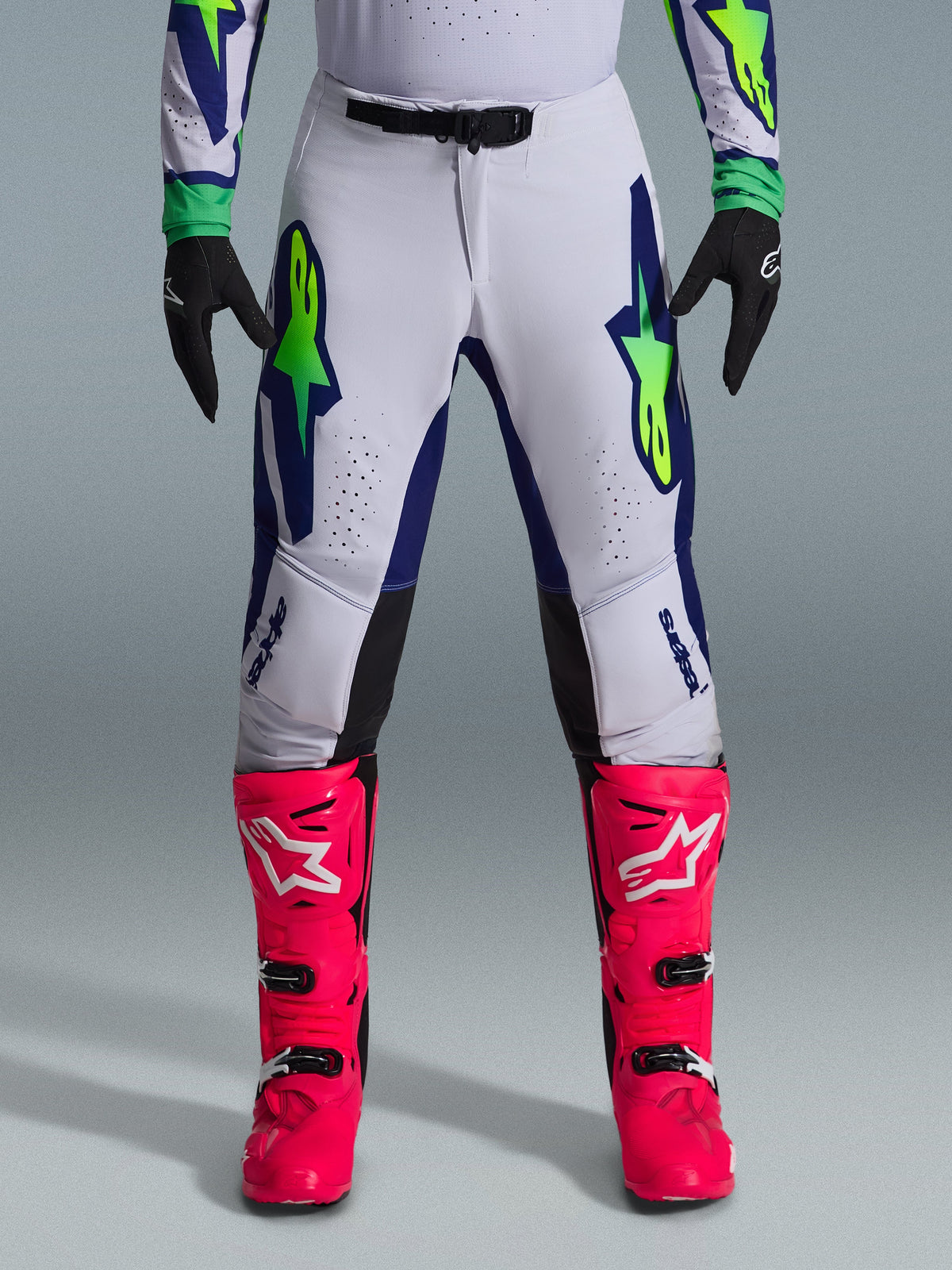 Alpinestars 2026 Supertech Vista Gear Set, motorcrossbroek in wit met blauwe en limoengroene accenten, gecombineerd met felroze laarzen en zwarte handschoenen, professionele race-uitrusting met atletische pasvorm en lasergesneden perforaties.