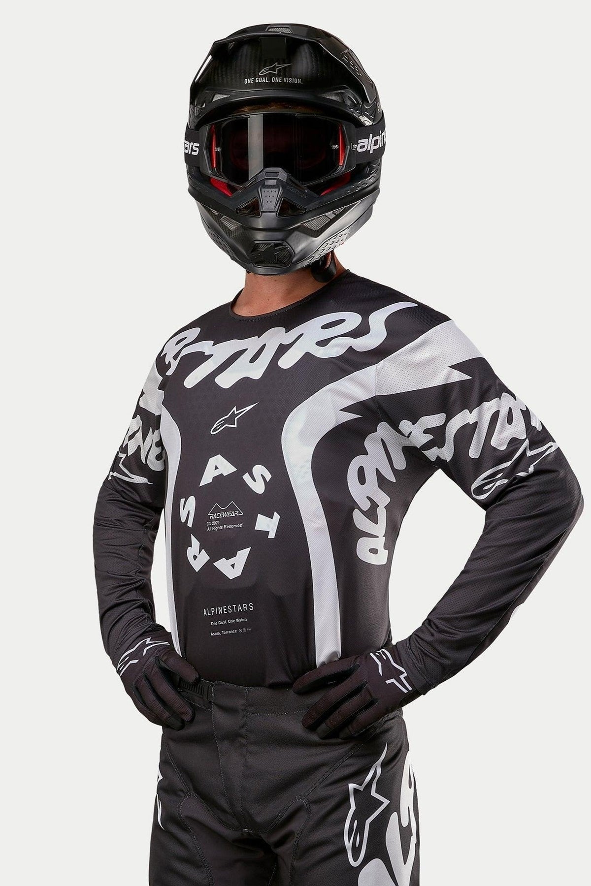 Alpinestars 2024 Racer Hana Jersey, motocross shirt, zwart en wit, voorzien van opvallende witte Alpinestars tekstgraphics en logo, gedragen door een rijder met een zwarte helm en crossbril, hoogwaardige uitrusting voor off-road racing