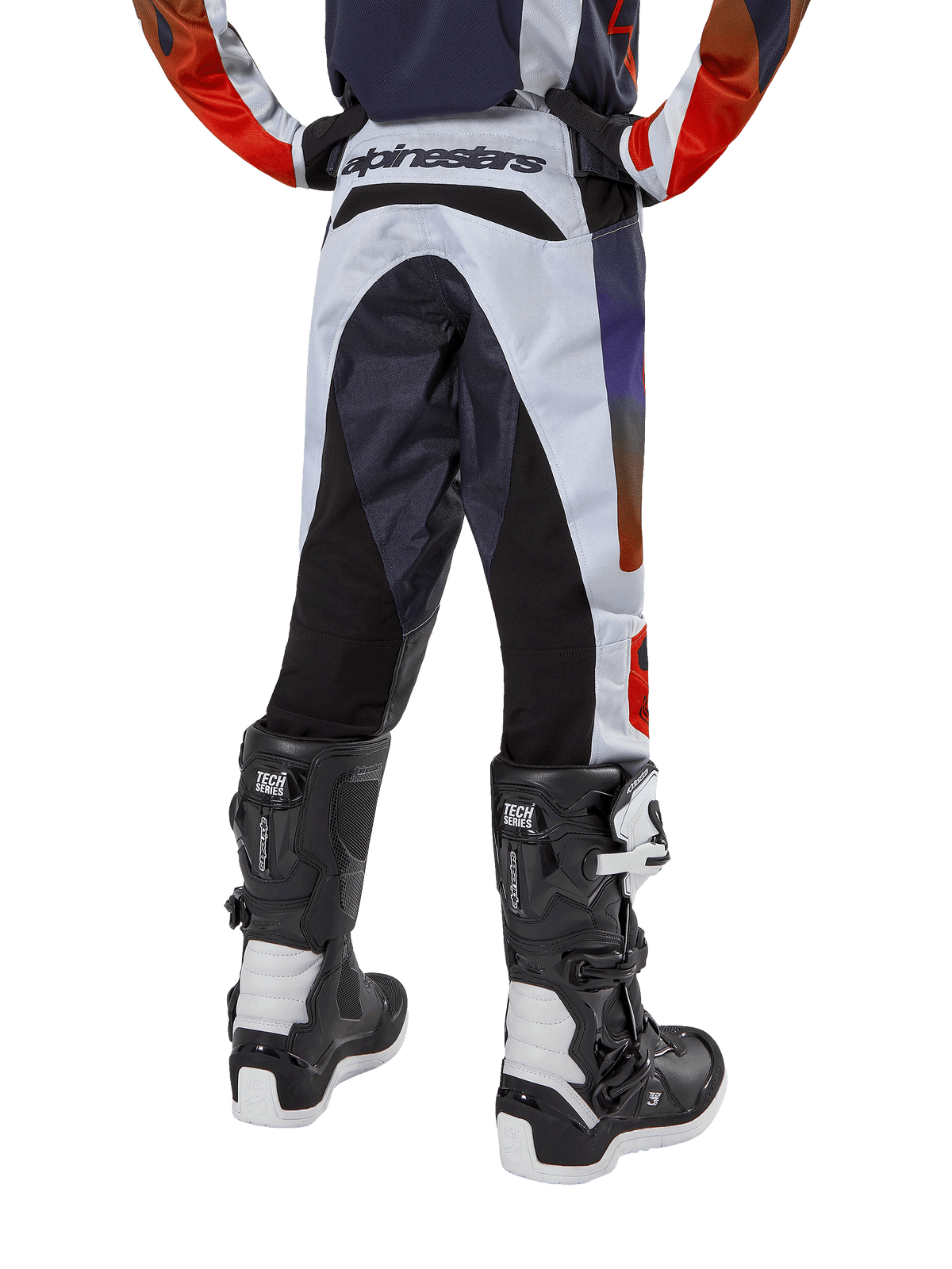 Alpinestars Youth 2024 Racer Hoen Pants, jeugd motorcrossbroek, lichtgrijs met feloranje en zwarte accenten, achteraanzicht met zwarte panelen op het zitvlak en de benen, opvallende merkdetails op de achterkant van de taille, gedragen met zwart-witte motorcrosslaarzen voor off-road rijden