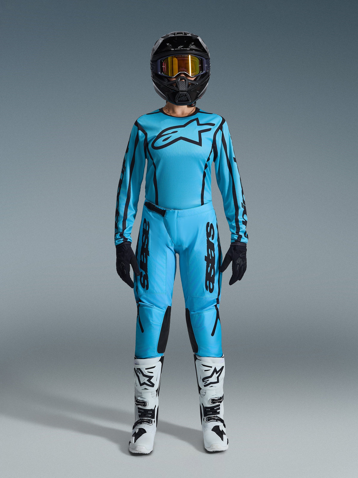 Alpinestars 2026 Stella Fluid Apex gear set, motocross jersey en broek voor dames, blauw en zwart, met een groot sterlogo op de borst, gedragen met een zwarte helm, getinte crossbril en witte laarzen met zwarte accenten, complete off-road race-outfit