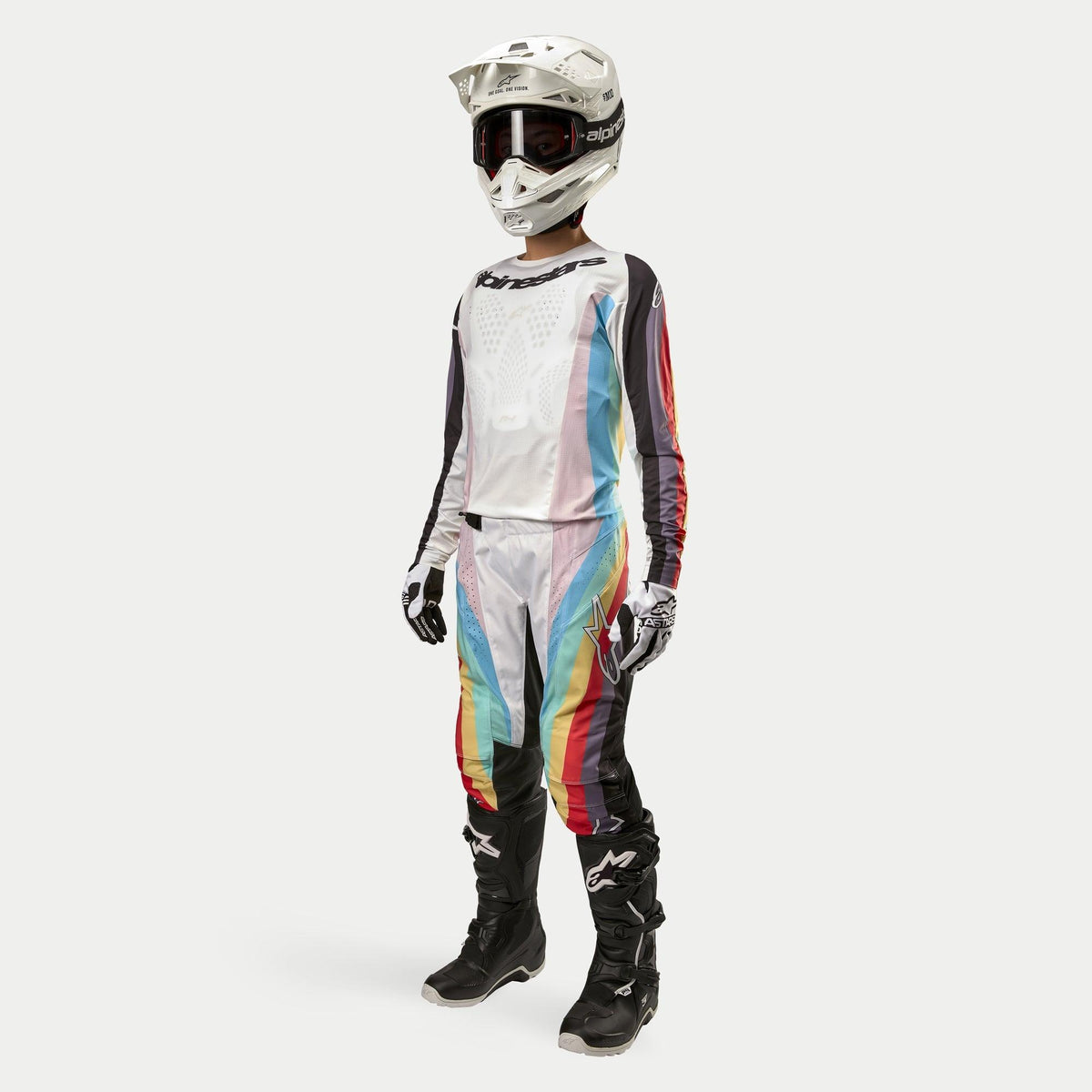Motorcrossrijder met Alpinestars Stella 2024 Techstar damesbroek, motorcrossbroek, Black Multicolor met witte panelen en levendige diagonale strepen, bijpassende jersey, witte helm en zwarte laarzen, gecoördineerde off-road race-outfit voor dames