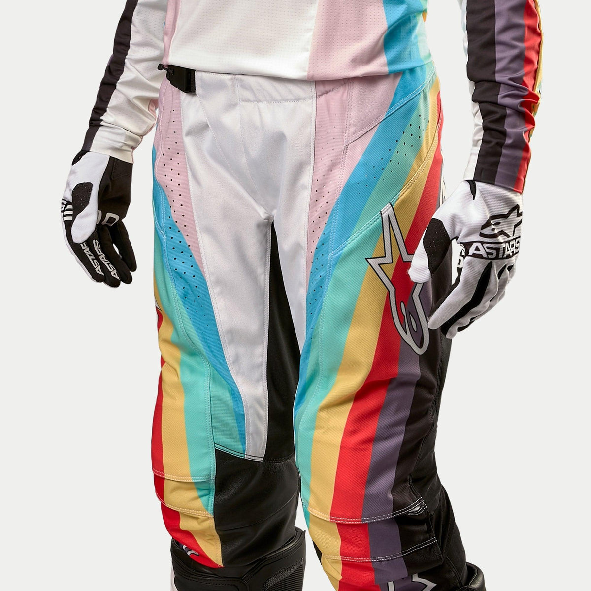 Alpinestars Stella Techstar crossbroek 2024 voor dames, motorcrossbroek, zwart meerkleurig met levendige diagonale strepen in blauw, roze, geel en rood, met een groot ster-logo op het dijbeen, gedragen met bijpassende jersey en handschoenen, professionele off-road race-uitrusting