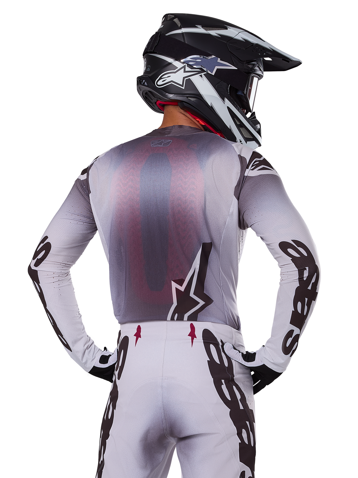 Motocrosser van achteren die de Alpinestars 2025 Supertech Maker Jersey draagt, zilver en zwart met een rood mesh rugpaneel en zwarte logo's op de mouwen, gecombineerd met een bijpassende motorcrossbroek en een zwart-witte helm, professionele off-road race-uitrusting