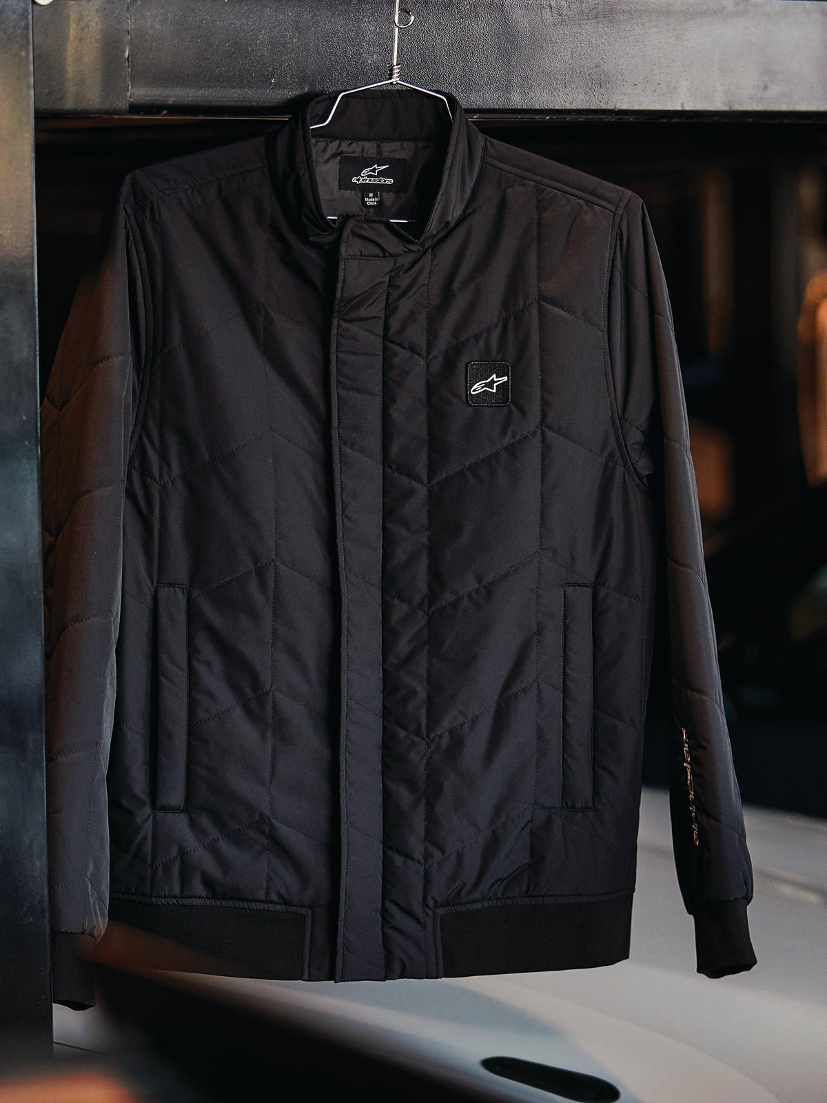 Alpinestars Precedent Jacket, Quilted Sportswear Jacket, Black, featuring an angled quilt pattern, low track collar with covered zipper, chest logo patch, and ribbed cuffs and hem, motorsport-inspired design