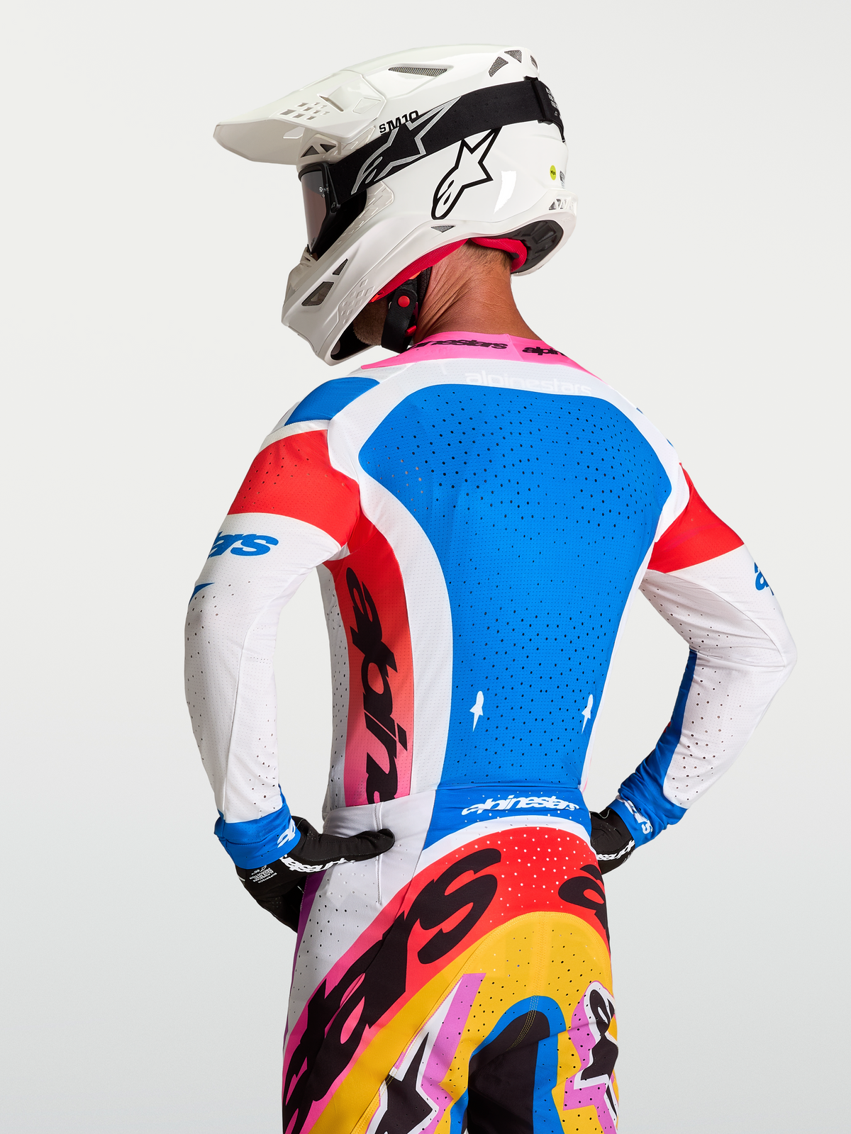 Alpinestars Supertech Dyna jersey, heren-motorcrossjersey in blauw en wit met roze accenten, atletisch stretchmesh met lasergesneden ventilatie, achteraanzicht van model met witte helm.