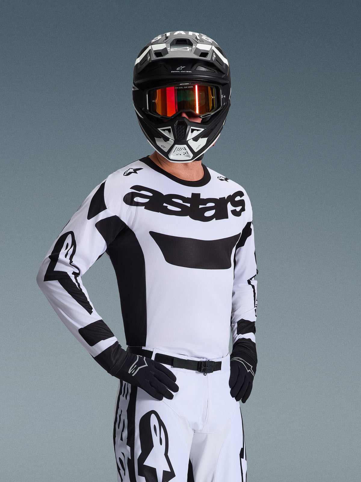 Alpinestars 2026 Racer Riway Jersey, motorcross jersey, wit en zwart, met opvallend 'astars' logo op de borst, gedragen met bijpassende witte broek en zwarte handschoenen, zwart-witte helm met rode reflecterende bril, professionele off-road race-uitrusting