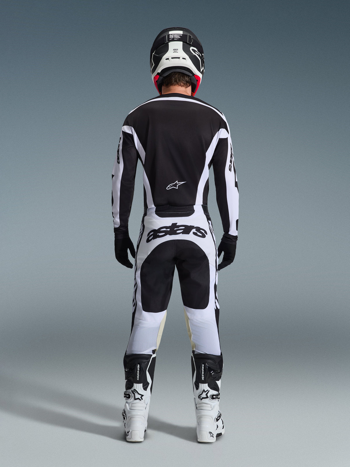 Motocrossrijder vanaf de achterkant in volledige race-uitrusting, 2026 Racer Riway Jersey in wit en zwart, bijpassende broek met 'astars' branding op het zitvlak, zwarte helm met witte details, zwarte handschoenen en wit-zwarte laarzen, gecoördineerde professionele off-road outfit
