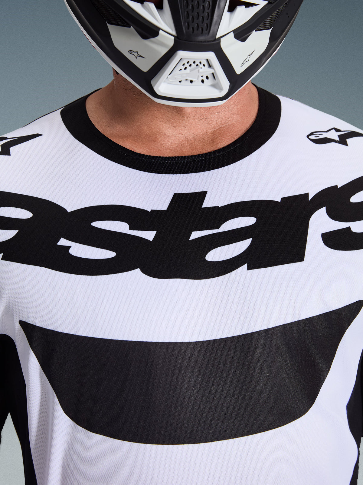 Close-up of a rider wearing the Alpinestars 2026 Racer Riway Jersey in White and Black, featuring bold 'astars' branding across the chest and a black crew neck collar, paired with a matching motocross helmet.