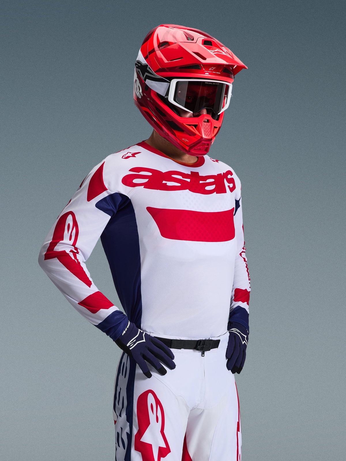 Motorcrosser die de Alpinestars 2026 Racer Riway Jersey in wit, blauw en rood draagt, met opvallende rode 'astars' branding op de borst en blauwe zijpanelen, gecombineerd met een bijpassende rode helm en witte racebroek voor een complete off-road performance look.