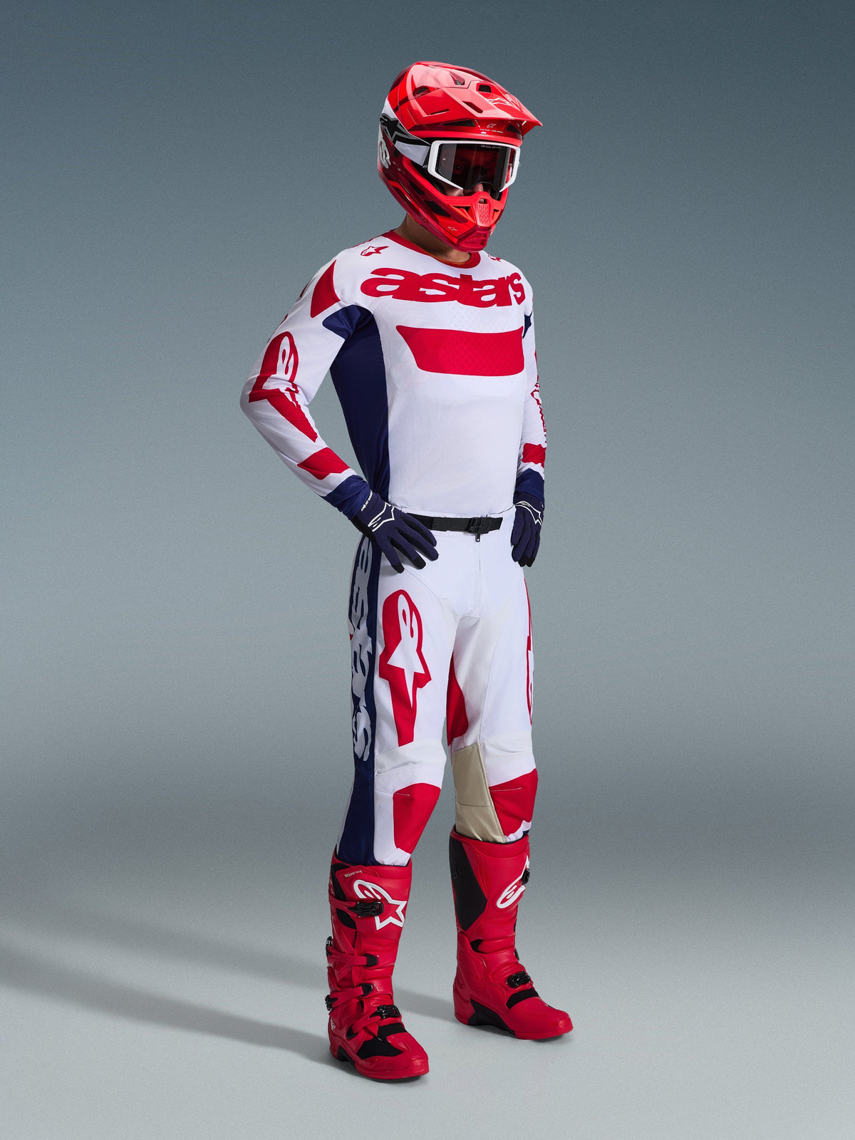 Motorcrosser met de 2026 Racer Riway Jersey in White Blue Red, bijpassende wit-rode broek, rode helm met witte crossbril, navy handschoenen en rode motorcrosslaarzen, complete race-uitrusting voor off-road prestaties.