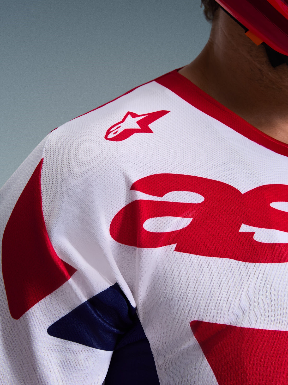 Detailopname van de Alpinestars 2026 Racer Riway Jersey in wit, blauw en rood, met de nadruk op de ademende mesh polyfabric constructie, het rode Alpinestars logo op de schouder en het vochtafvoerende materiaal voor off-road racing.