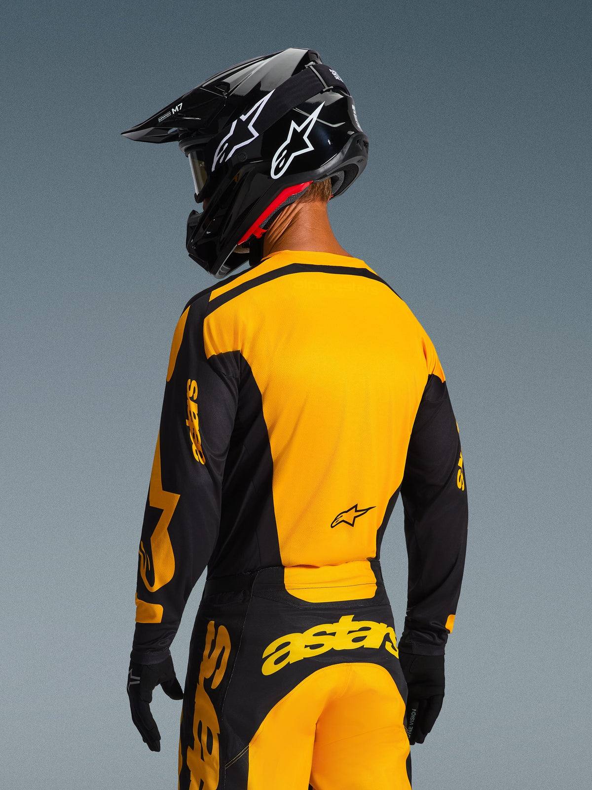 Motorcrossrijder van achteren gezien die de 2026 Racer Riway Jersey en bijpassende broek in geel en zwart draagt, met opvallende Alpinestars-branding, een zwarte helm met witte sterlogo's en zwarte handschoenen, een gecoördineerde motorcross-set voor off-road racen.