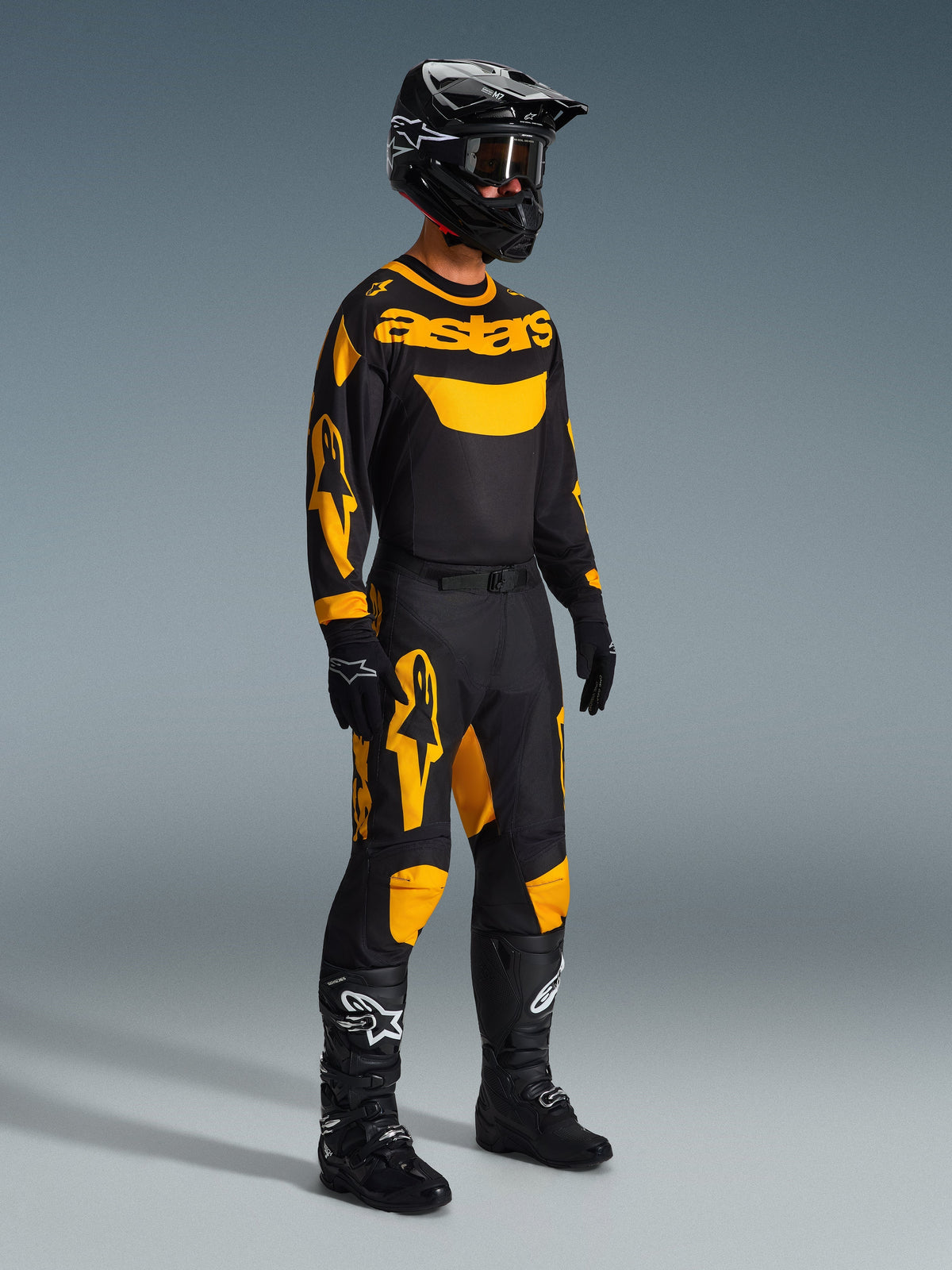 Motorcrosser in volledige race-uitrusting, Alpinestars 2026 Racer Riway Jersey in geel en zwart, bijpassende zwart-gele broek, zwarte helm met crossbril, zwarte laarzen en handschoenen, geco''rdineerde outfit voor off-road racen