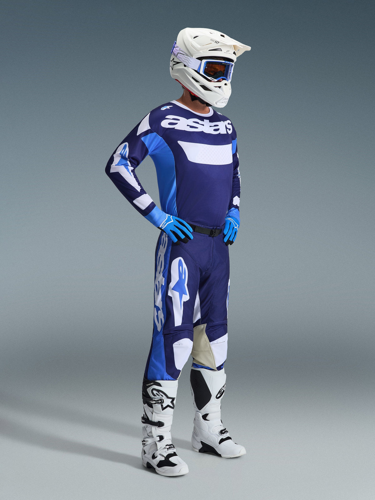 Alpinestars 2026 Racer Riway Jersey in Ucla Blue en wit, gedragen door een motorcrosser met bijpassende broek, witte helm, blauwe handschoenen en witte laarzen, voorzien van opvallende 'astars' branding op de borst, complete off-road race-outfit