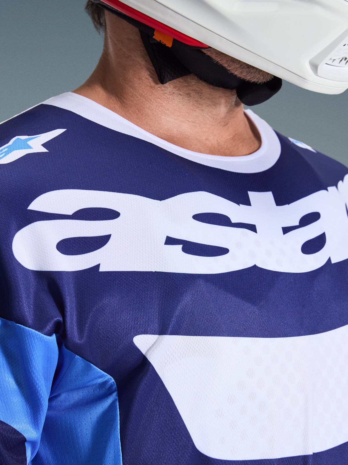 Close-up van Alpinestars 2026 Racer Riway Jersey in Ucla Blue en wit, met een groot wit 'astars'-logo op de borst, witte kraag en ademende mesh-stoftextuur, gedragen met een witte motorcrosshelm