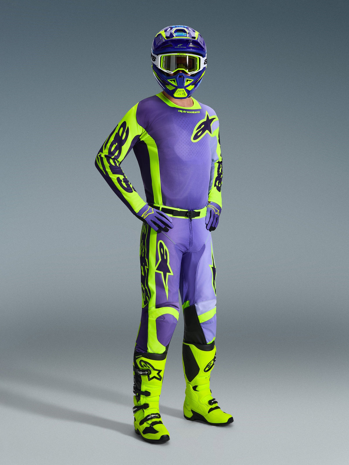 Motocrosser in een complete Alpinestars uitrusting, met de 2026 Racer Portl Jersey en bijpassende broek in paars en fluo geel, gecoördineerd met een bijpassende helm, bril en paarse handschoenen, afgewerkt met felgele fluo off-road laarzen, een professionele race-outfit voor motorcross-prestaties.
