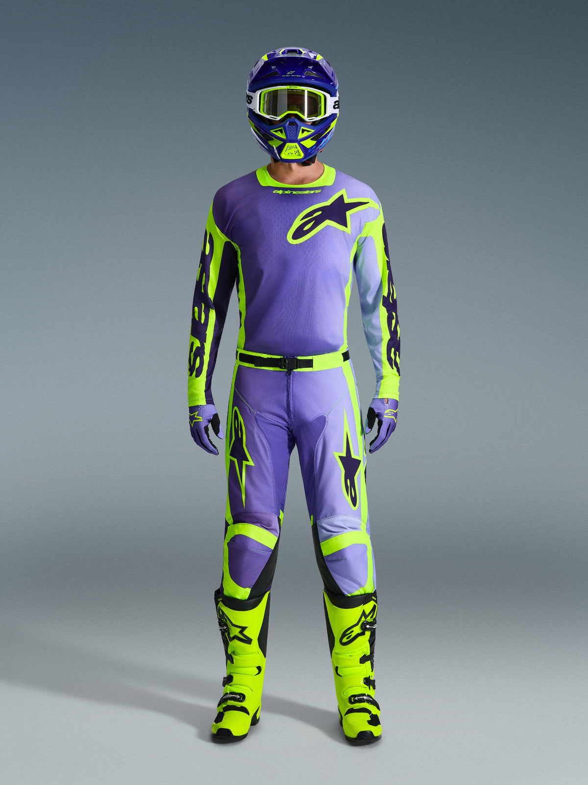 Alpinestars 2026 Racer Portl Jersey, paars en fluo geel, gedragen als onderdeel van een complete motorcross-uitrusting met bijpassende broek, helm en fel neongele laarzen, professionele off-road race-outfit.
