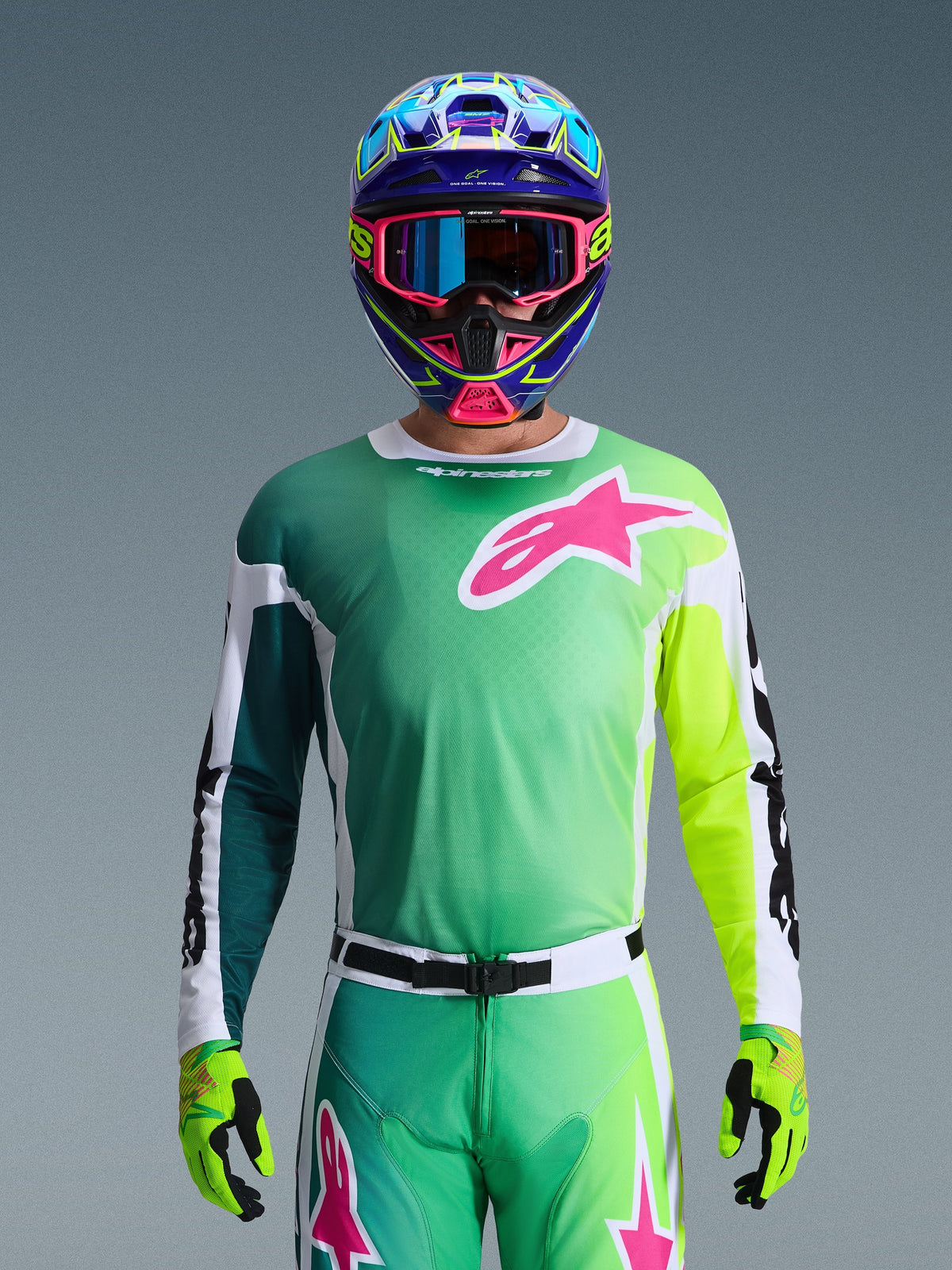 Alpinestars 2026 Racer Portl Jersey, motorcross shirt, groen, wit en zwart met een groot roze Alpinestars-logo op de borst, gedragen door een rijder met een levendige meerkleurige helm en bijpassende bril, professionele off-road racekleding