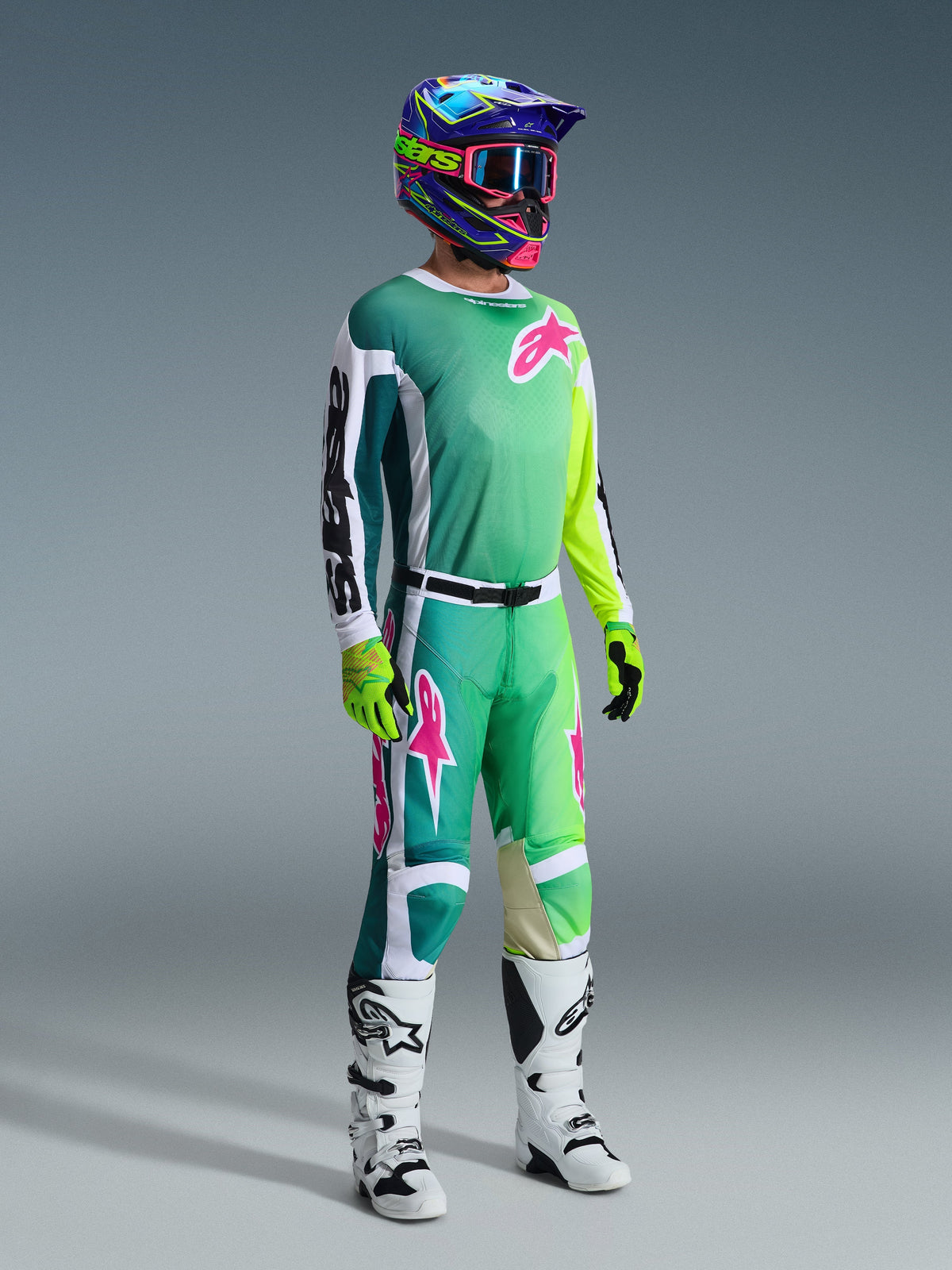 Motorcrossrijder in volledige race-uitrusting, 2026 Racer Portl Jersey in het groen met witte en zwarte mouwen en roze logo, bijpassende groene broek met roze accenten, veelkleurige helm met crossbril, wit-zwarte laarzen en groene handschoenen, gecoördineerde outfit voor off-road racing