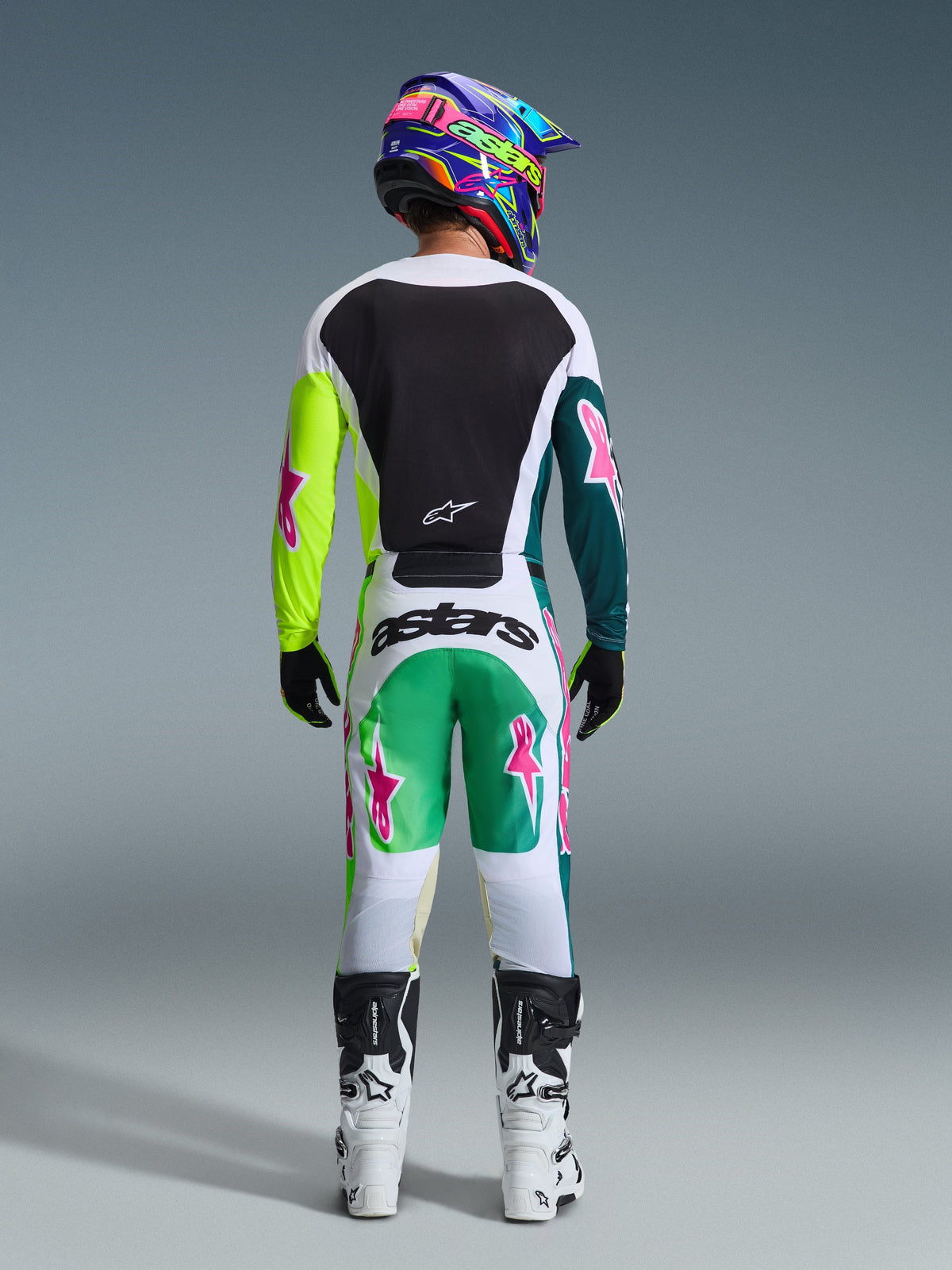 Motorcrosser van achteren gezien in de 2026 Racer Portl Jersey in Green White Black, voorzien van een zwart rugpaneel en asymmetrische groene mouwen met roze ster-logo's, gecombineerd met een bijpassende motorcrossbroek en witte laarzen.
