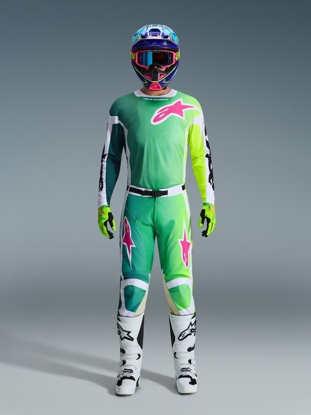 Motorcrosser in de Alpinestars 2026 Racer Portl Jersey in groen, wit en zwart, voorzien van opvallende roze en limoengroene accenten en een groot roze sterlogo op de borst, gecombineerd met een bijpassende broek, een kleurrijke helm, limoengroene handschoenen en witte motorcrosslaarzen, complete race-uitrusting.