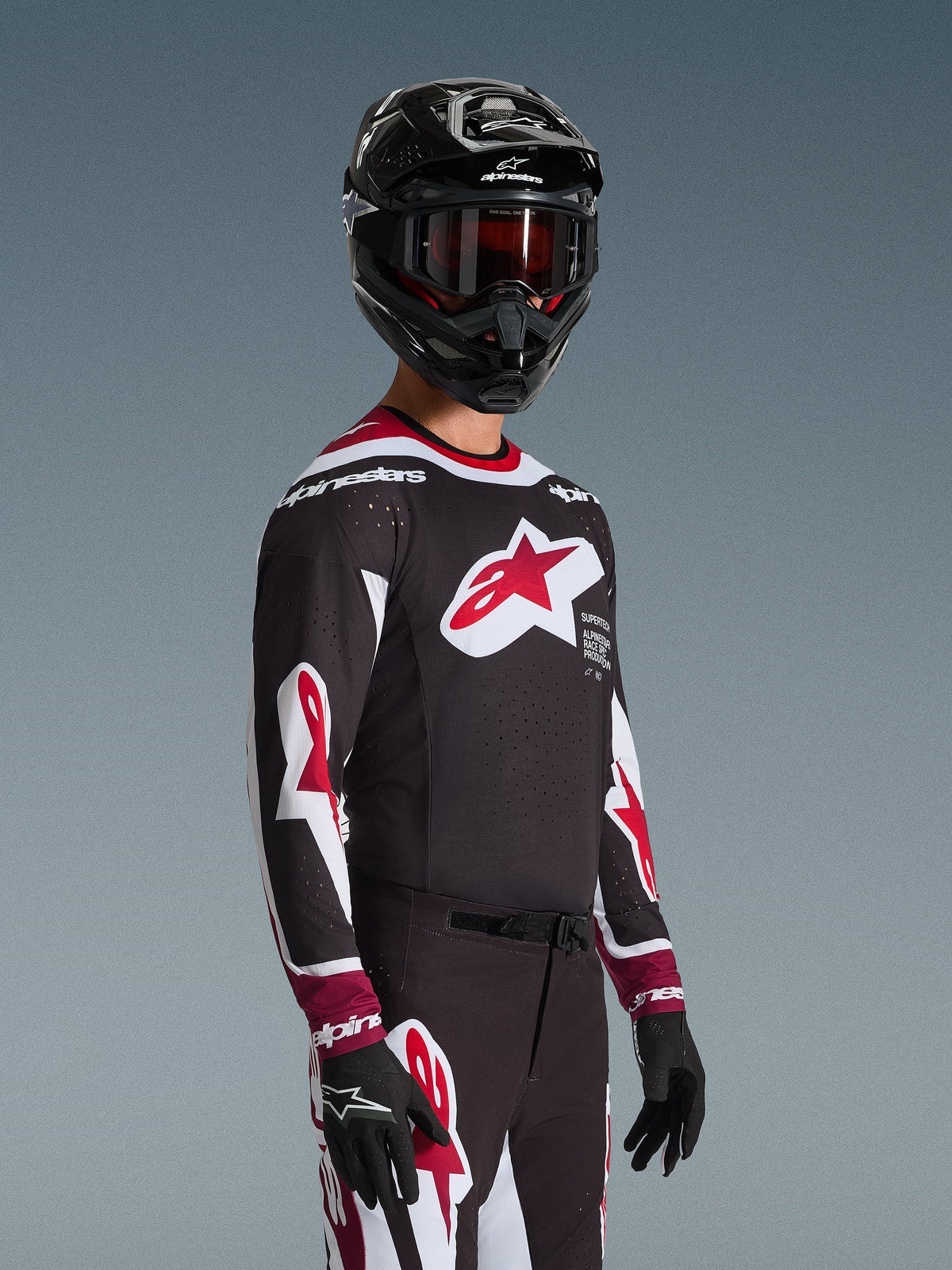 Alpinestars 2026 Supertech AFD Vista Jersey, motorcrosser in volledige race-uitrusting, zwarte jersey met rode en witte accenten, groot logo op de borst, lasergesneden perforaties, gecombineerd met bijpassende broek, zwarte helm en rode bril, complete outfit voor off-road racen