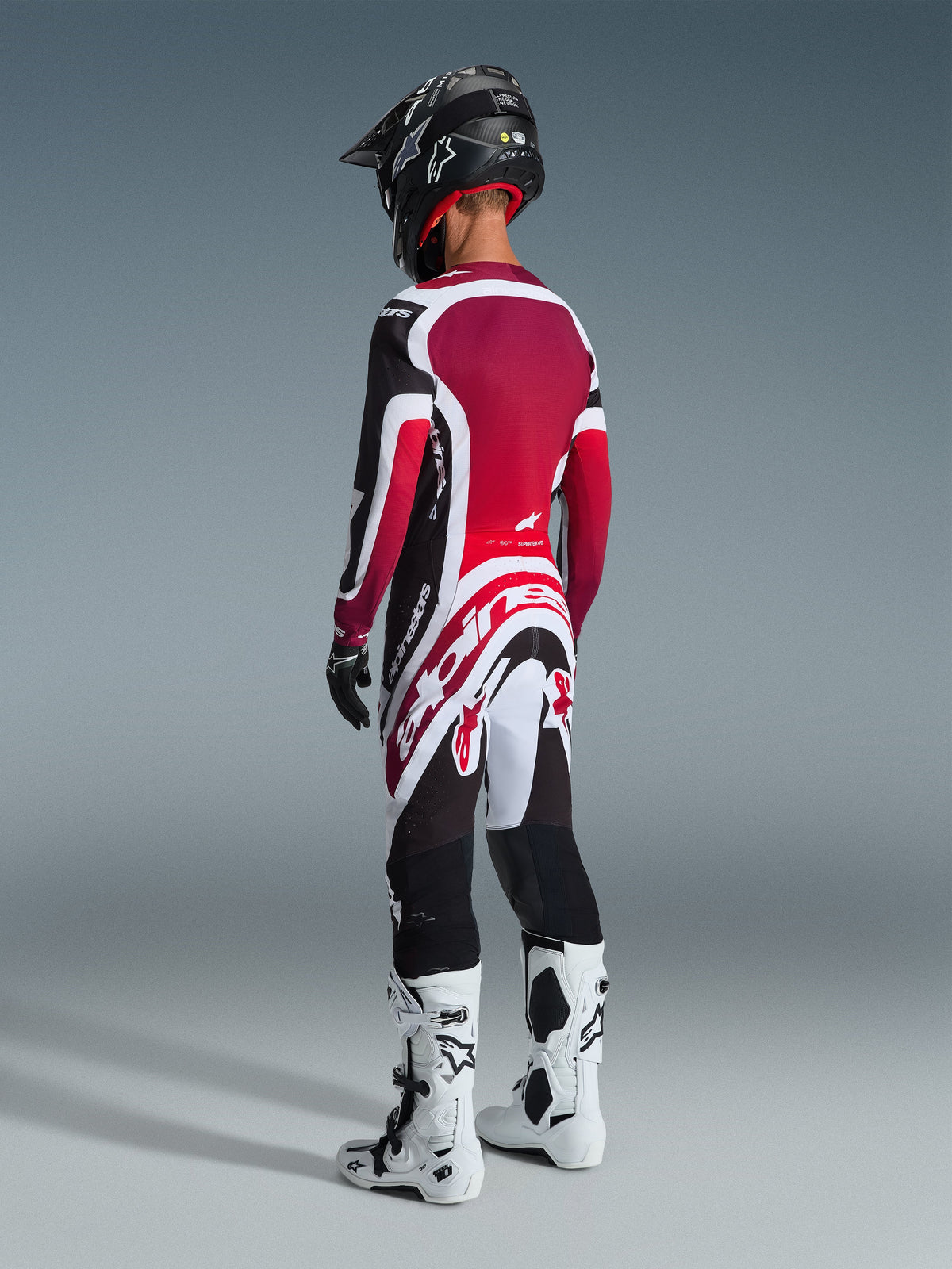 Motocrossrijder van achteren gezien in de Alpinestars 2026 Supertech AFD Vista Gear Set, rood, wit en zwart shirt en broek met opvallende Alpinestars-branding, zwarte helm, wit-zwarte laarzen en zwarte handschoenen voor een complete professionele race-uitstraling.