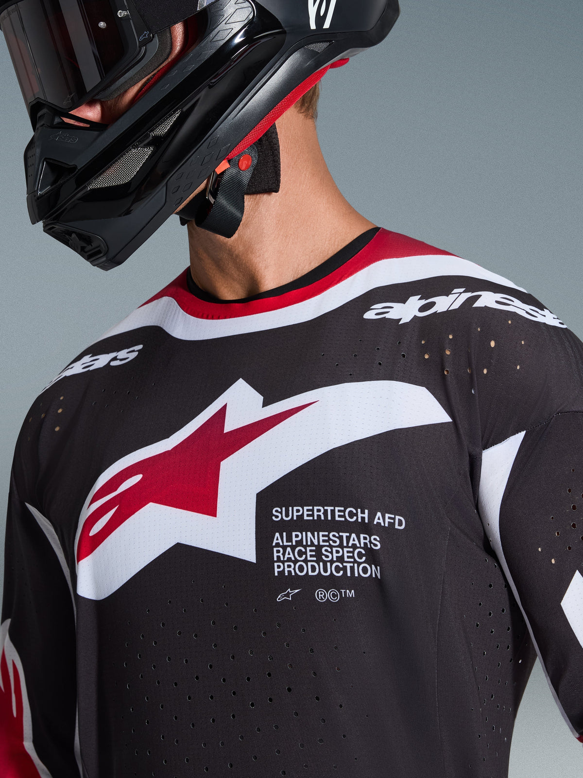 Alpinestars 2026 Supertech AFD Vista Jersey, zwart, rood en wit, close-up van de borst met het Alpinestars sterlogo en 'Supertech AFD' tekst, voorzien van lasergesneden ventilatiegaten en mesh-constructie, gedragen met een zwarte motorcrosshelm.