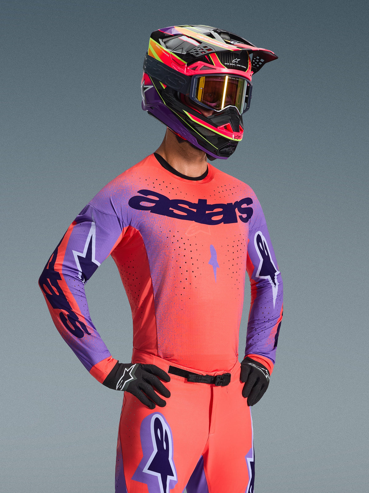 Motocrossrijder in de Alpinestars 2026 Supertech Scenz Jersey, Hot Coral en paars met opvallend 'astars' logo op de borst, inclusief bijpassende koraalrode broek en paars-koraalrode helm, voorzien van laser-gesneden perforaties voor high-performance off-road racing.