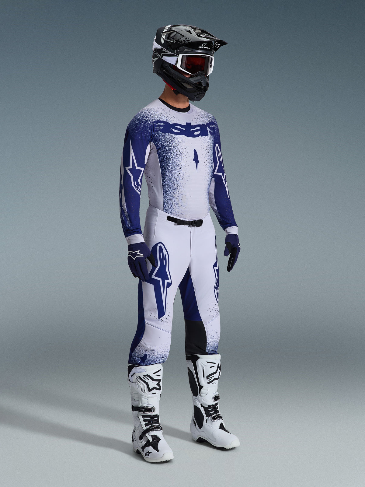 Alpinestars 2026 Supertech Scenz Gear Set, motorcrosser in wit en marineblauw race-shirt en broek met een gradiënt stippeleffect, voorzien van opvallende Astars-branding, gecombineerd met een zwart-witte helm, marineblauwe handschoenen en witte motorcrosslaarzen.