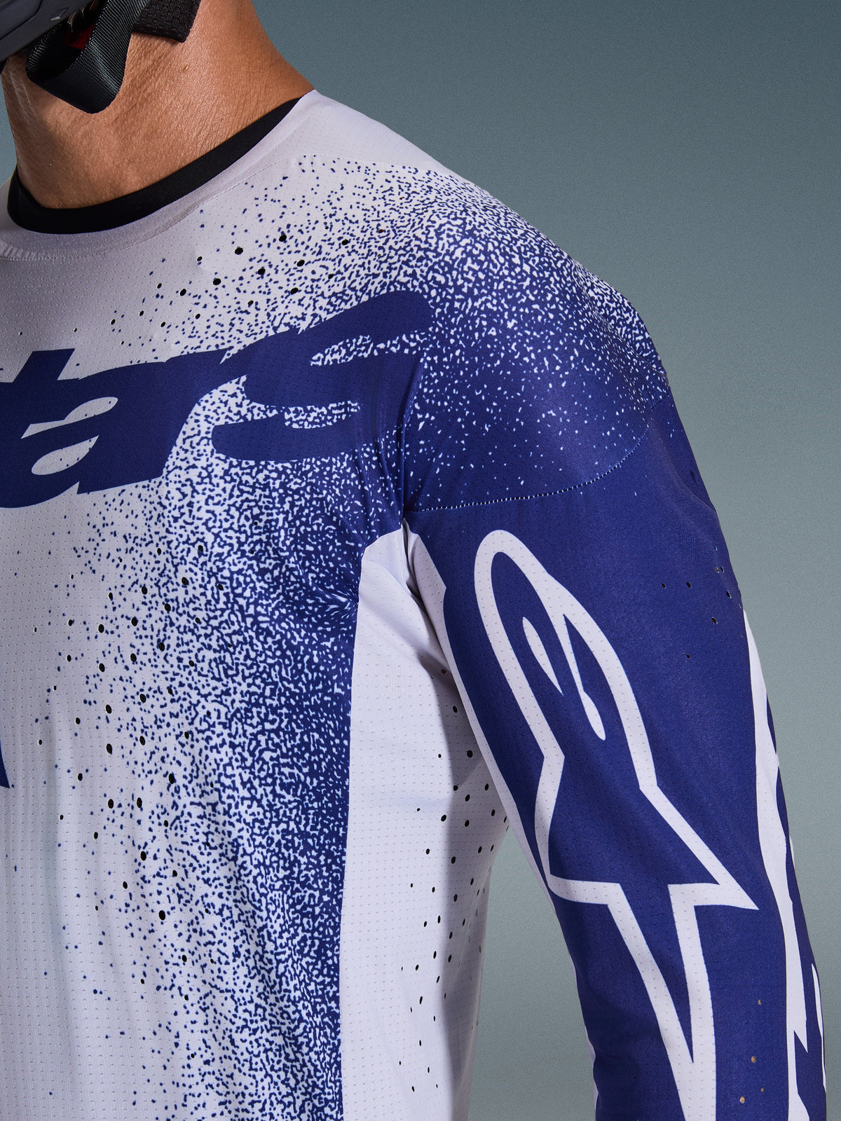 Alpinestars 2026 Supertech Scenz Jersey, lichtgrijs en donkerblauw, close-up van de schouder en borst met laser-gesneden perforaties, wit Astars-logo op de blauwe mouw, gespikkeld grafisch ontwerp, professionele motorcross race-uitrusting