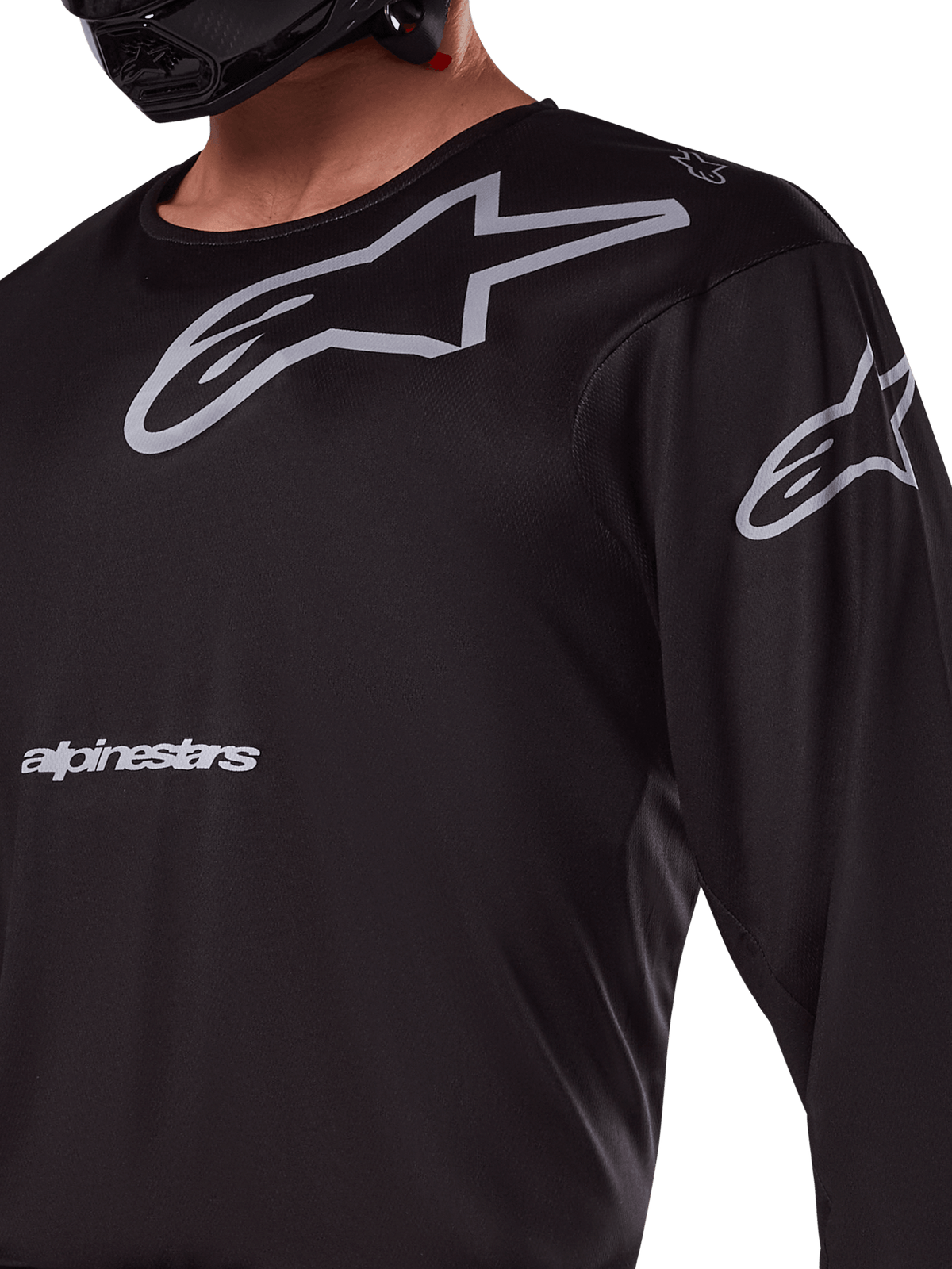 Alpinestars 2025 Racer Graphite Jersey, zwart en grijs, close-up van rijder die motocross jersey draagt, met grijze Alpinestars-branding en A-star-logo's, technisch poly-materiaal voor off-road rijden