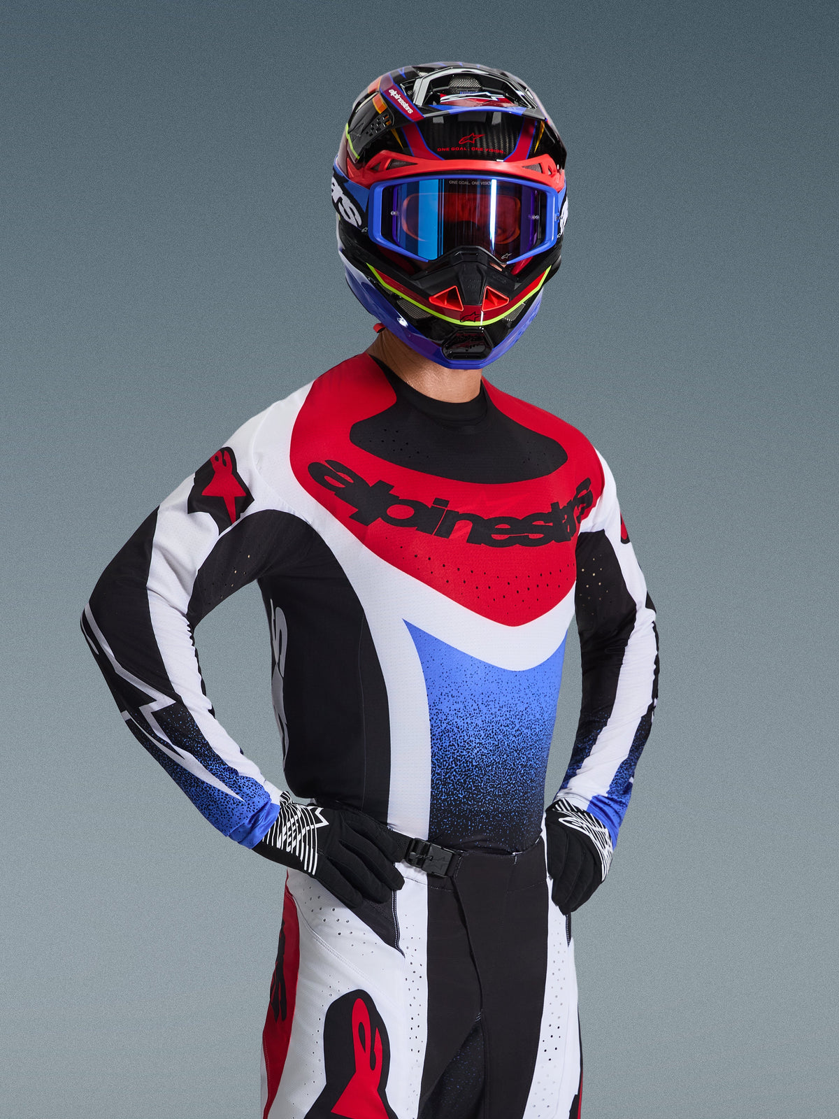 Alpinestars 2026 Techstar Knif Gear Set, motorcrossrijder in een rood, wit en blauw motorcross-jersey met zwarte accenten, bijpassende meerkleurige helm en crossbril, zwarte handschoenen, professionele uitrusting voor motorcrosswedstrijden.