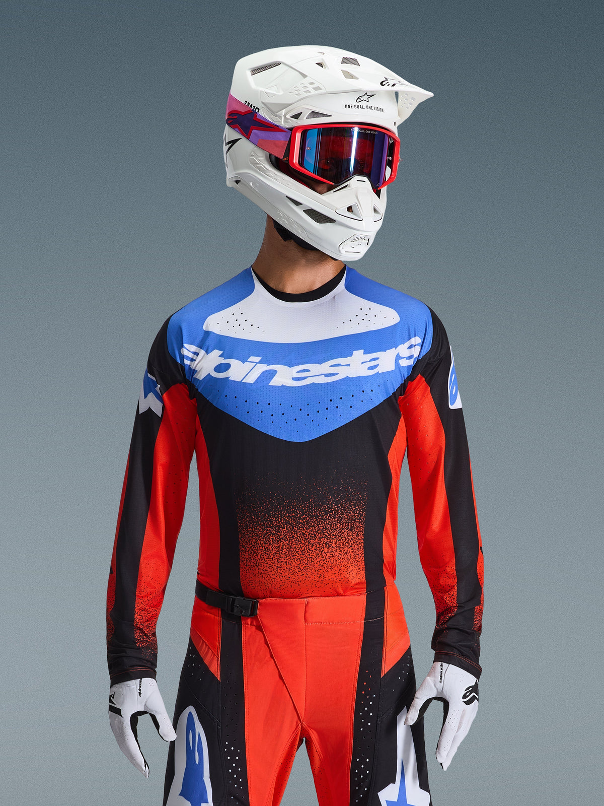 Alpinestars 2026 Techstar Knif Gear Set, motorcross race-uitrusting met een blauw, wit, zwart en rood shirt met Alpinestars-branding, bijpassende rode en zwarte broek, gedragen met een witte helm, rode bril en witte handschoenen, atletische prestatiepasvorm voor off-road competitie