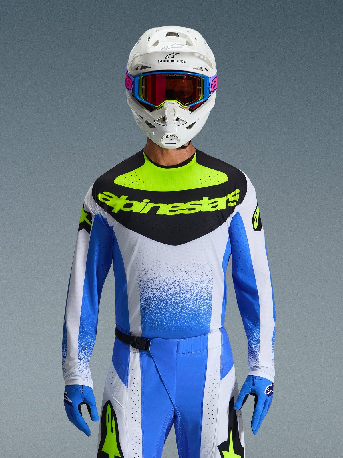 Alpinestars 2026 Techstar Knif Gear Set, motorcrossrijder in blauwe, witte en neongele racekleding, jersey met een zwart borstpaneel en neongele branding, witte helm met veelkleurige crossbril, bijpassende blauwe handschoenen en broek, hoogwaardige sportieve race-outfit voor off-road competitie