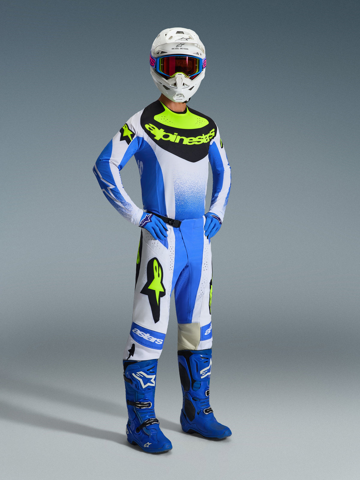 Alpinestars 2026 Techstar Knif Gear Set, complete motorcross outfit in UCLA Blue, zwart en fluorgeel, met performance jersey, bijpassende crossbroek, blauwe laarzen en handschoenen, witte helm met crossbril, grijze achtergrond