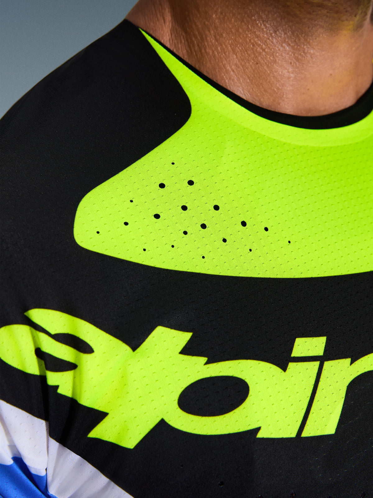 Alpinestars 2026 Techstar Knif Jersey, close-up van motorcross shirt in zwart en geel fluo, details van lasergesneden perforaties voor ventilatie, naadloos gelijmde kraag en vochtafvoerende stof met geel logo.