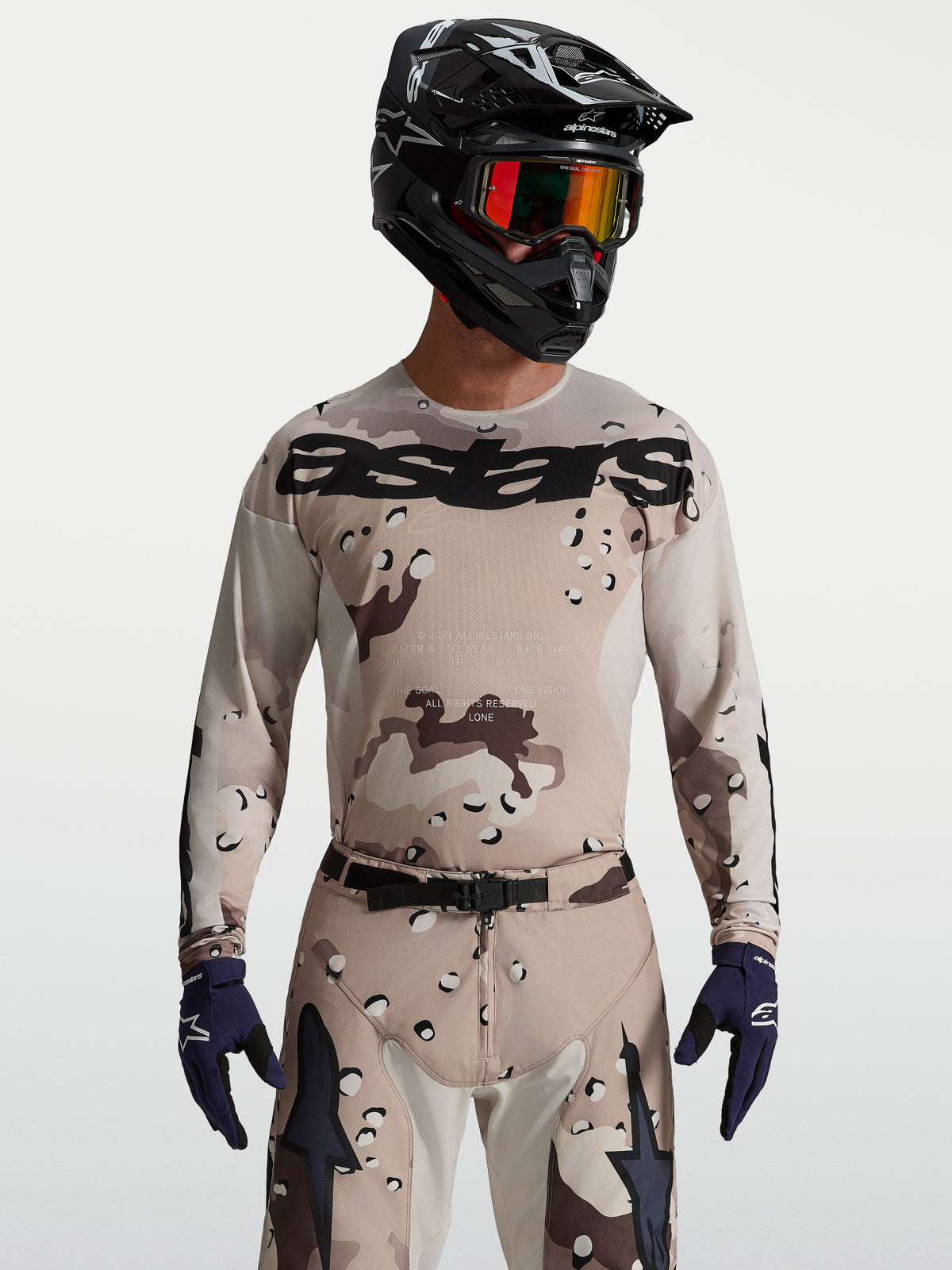 Alpinestars Racer Lone Jersey, heren-motocrossjersey in desert camo en zwart, op model met helm en veiligheidsbril.