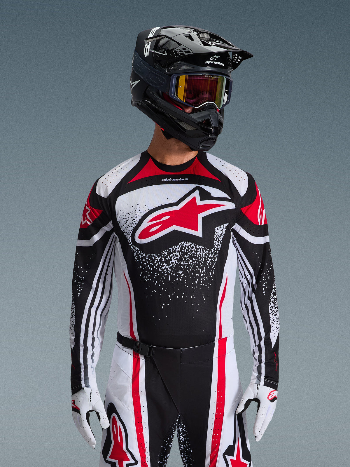 Alpinestars 2026 Techstar Nomur Gear Set, Motocross Jersey and Pants, Black White and Red, featuring a large red logo on the chest with a speckled graphic design, worn with a black helmet, red goggles, and white gloves, professional athletic race fit for off-road racing.