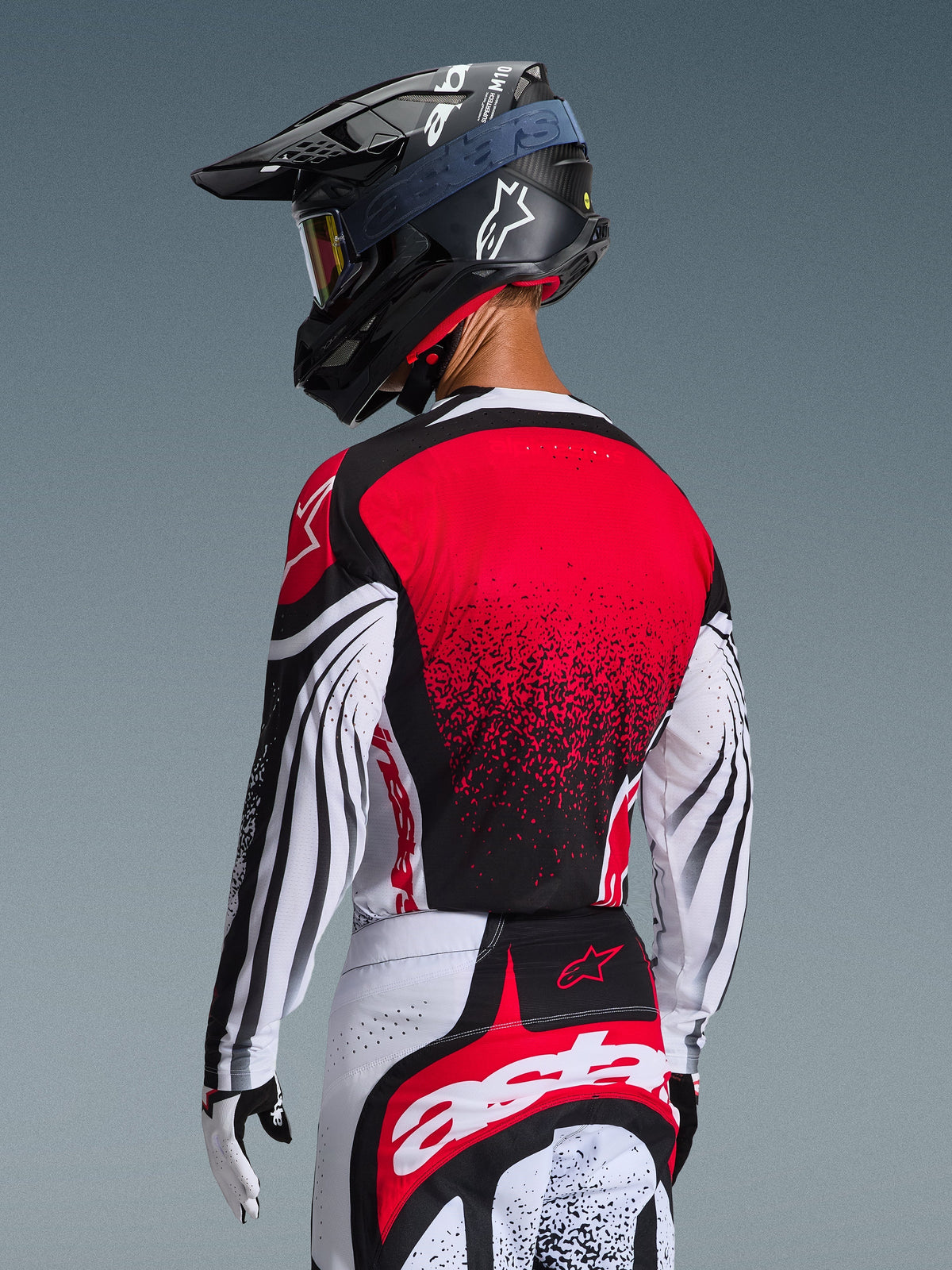 Motocross rider from behind wearing the 2026 Techstar Nomur Jersey, Red back with black gradient design and white sleeves with black accents, worn with matching red and white pants, black helmet, and white gloves, professional off-road racing gear