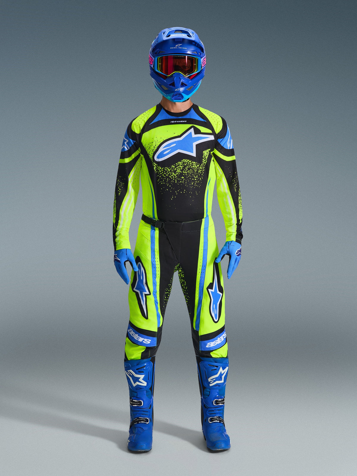 Motocross rider wearing complete racing gear, 2026 Techstar Nomur Jersey in yellow fluo and dark navy, matching motocross pants, blue helmet with red-tinted goggles, blue gloves, and blue boots, coordinated professional outfit for off-road racing