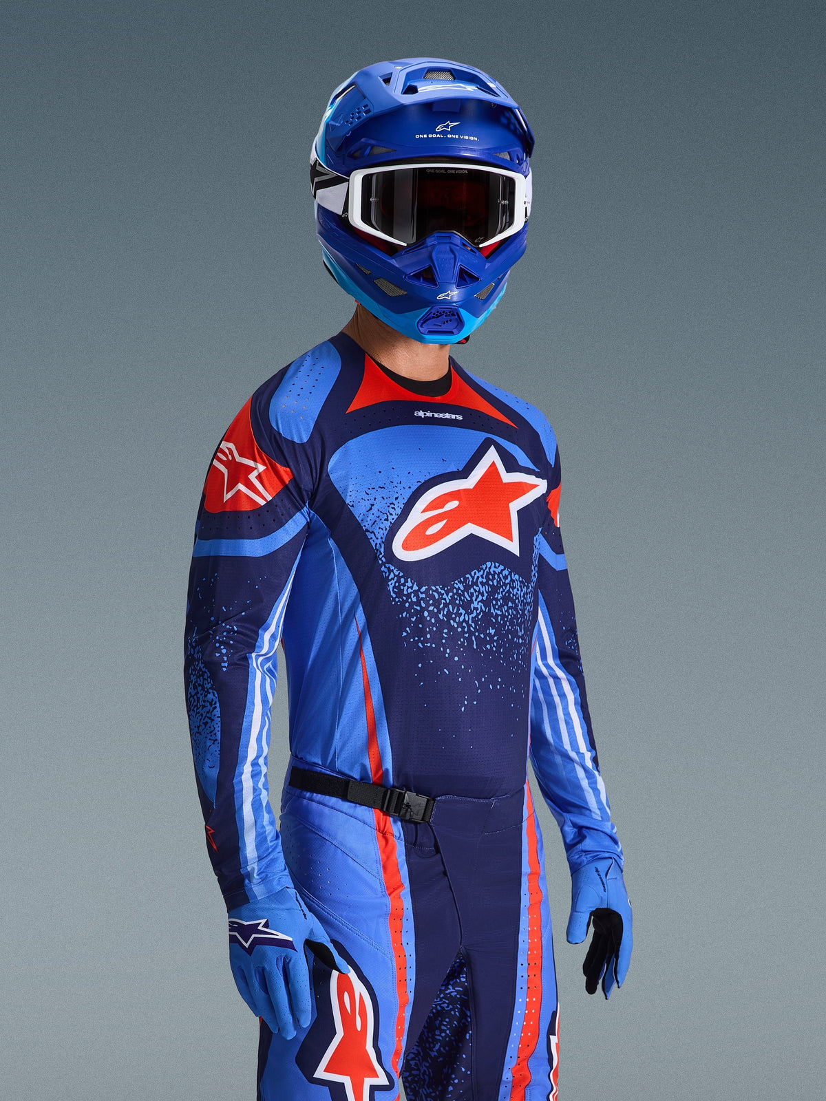 Motocross-rijder in Alpinestars 2026 Techstar Nomur Jersey, Dark Navy Orange en UCLA Blue race-uitrusting, met een groot oranje Astars-logo, bijpassende blauwe helm en handschoenen, atletische off-road wedstrijdoutfit.