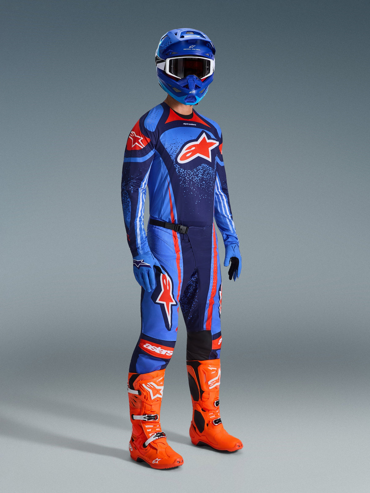 Motorcrosser in volledige race-uitrusting, blauw en donkerblauw Techstar Nomur Jersey met oranje Alpinestars-logo, bijpassende blauwe en donkerblauwe broek met oranje accenten, blauwe helm met witte crossbril, feloranje laarzen en blauwe handschoenen, gecoördineerde outfit voor off-road racen