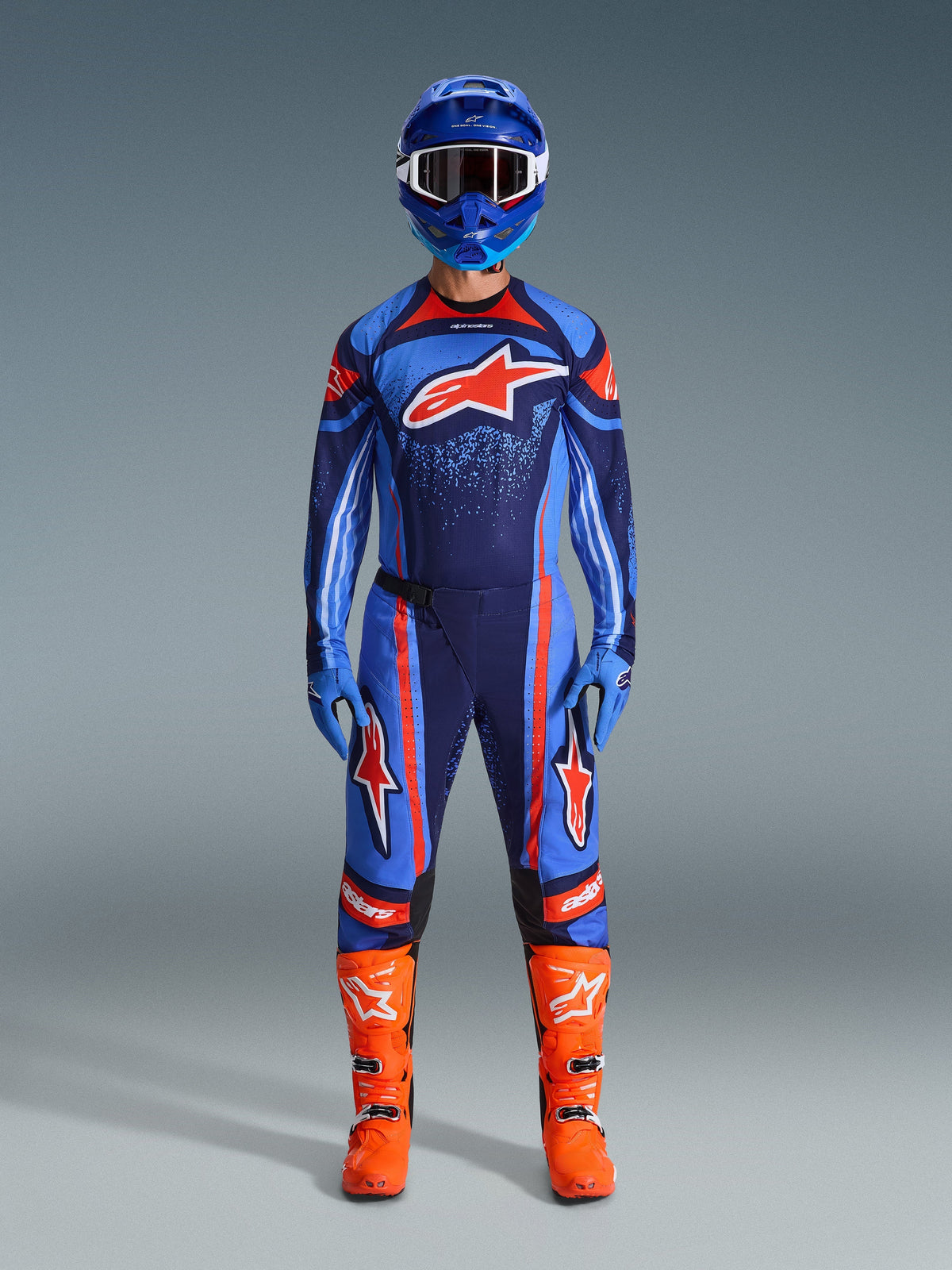 Motorcrosser in het Alpinestars 2026 Techstar Nomur Jersey in Dark Navy, oranje en UCLA Blue, gecombineerd met een bijpassende crossbroek, een blauwe helm met crossbril en feloranje racelaarzen, volledige gecoördineerde off-road wedstrijduitrusting