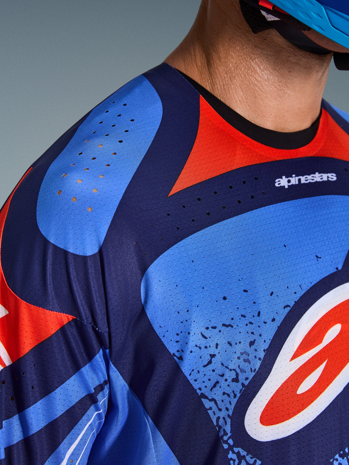 Close-up van Alpinestars 2026 Techstar Nomur Jersey, motorcross shirt, donkerblauw, oranje en UCLA-blauw, voorzien van laser-gesneden ventilatiegaten op de schouder en borst, technisch vochtafvoerend materiaal, atletische racepasvorm