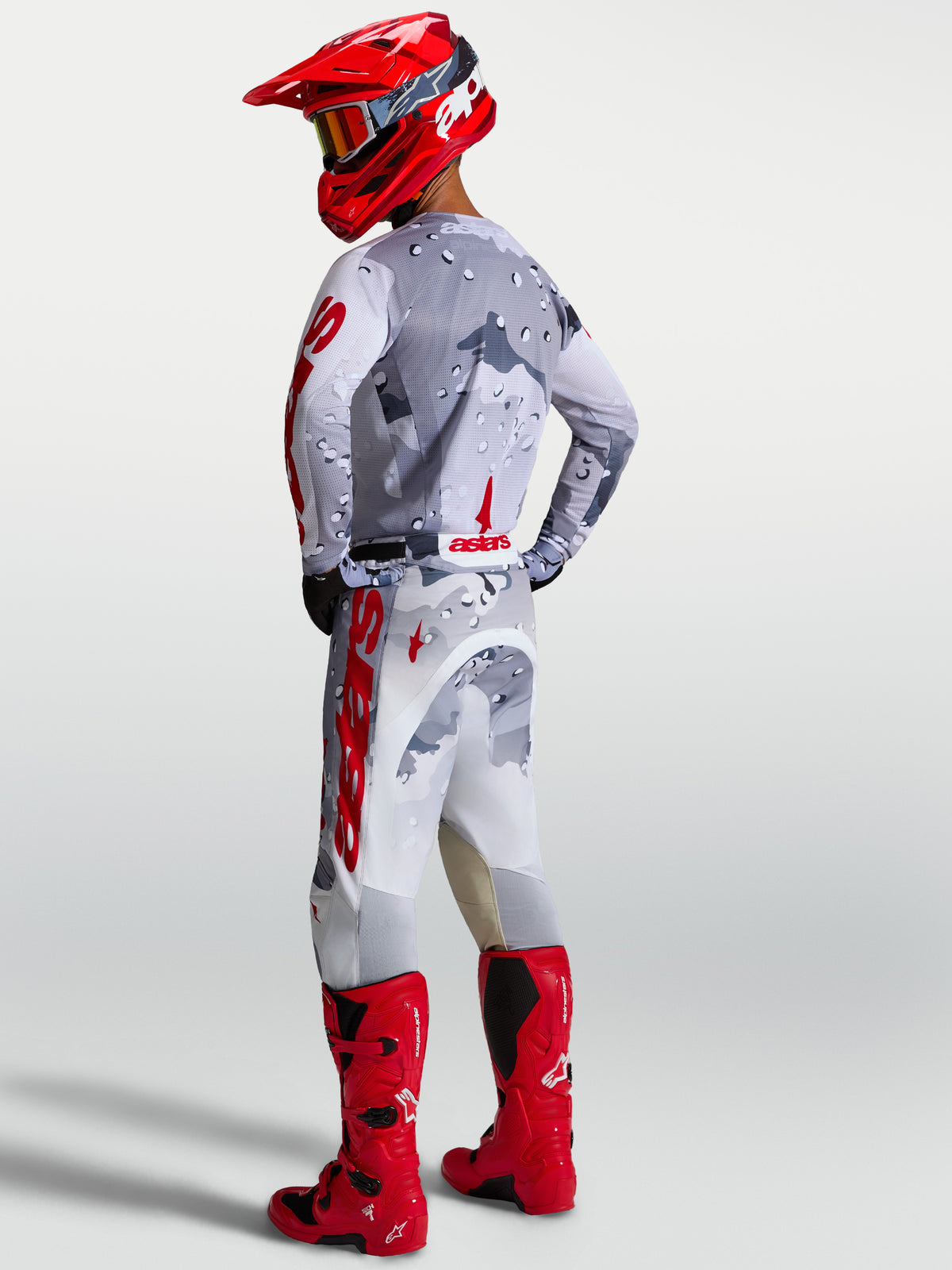 Alpinestars Racer Air Lone Jersey en broek, motorcrossuitrusting in grijs camo en rood, ademende meshconstructie voor warm weer, complete off-road set met rode motorlaarzen en helm.