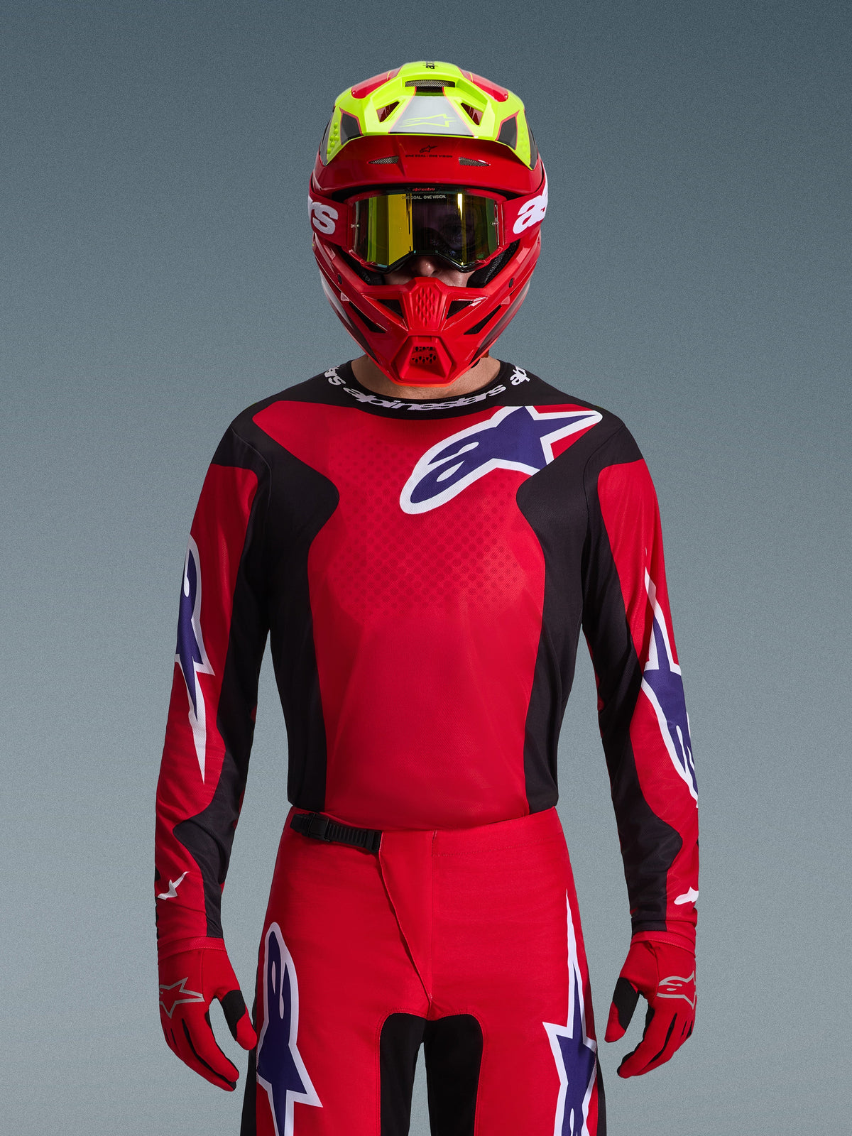 Alpinestars 2026 Fluid Grid Gear Set, motorcrossrijder in rode jersey met zwarte zijpanelen en wit sterlogo, bijpassende rode broek en handschoenen, rode en gele helm met goud getinte bril, hoogwaardige race-uitrusting voor off-road