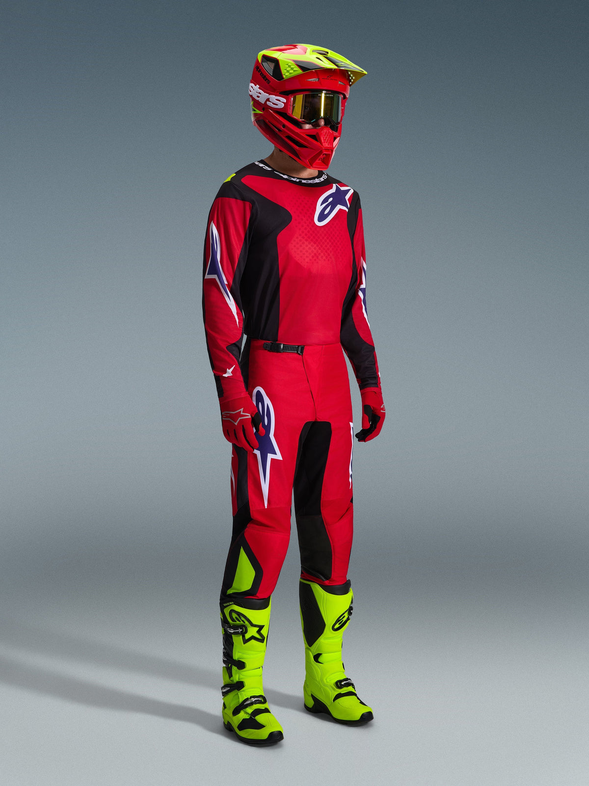 Alpinestars motorcrosser in volledige race-uitrusting, 2026 Fluid Grid Jersey in rood, zwart en paars, bijpassende broek met paarse logo-accenten, rode en neongele helm met gouden bril en neongele laarzen, gecoördineerde outfit voor off-road racing