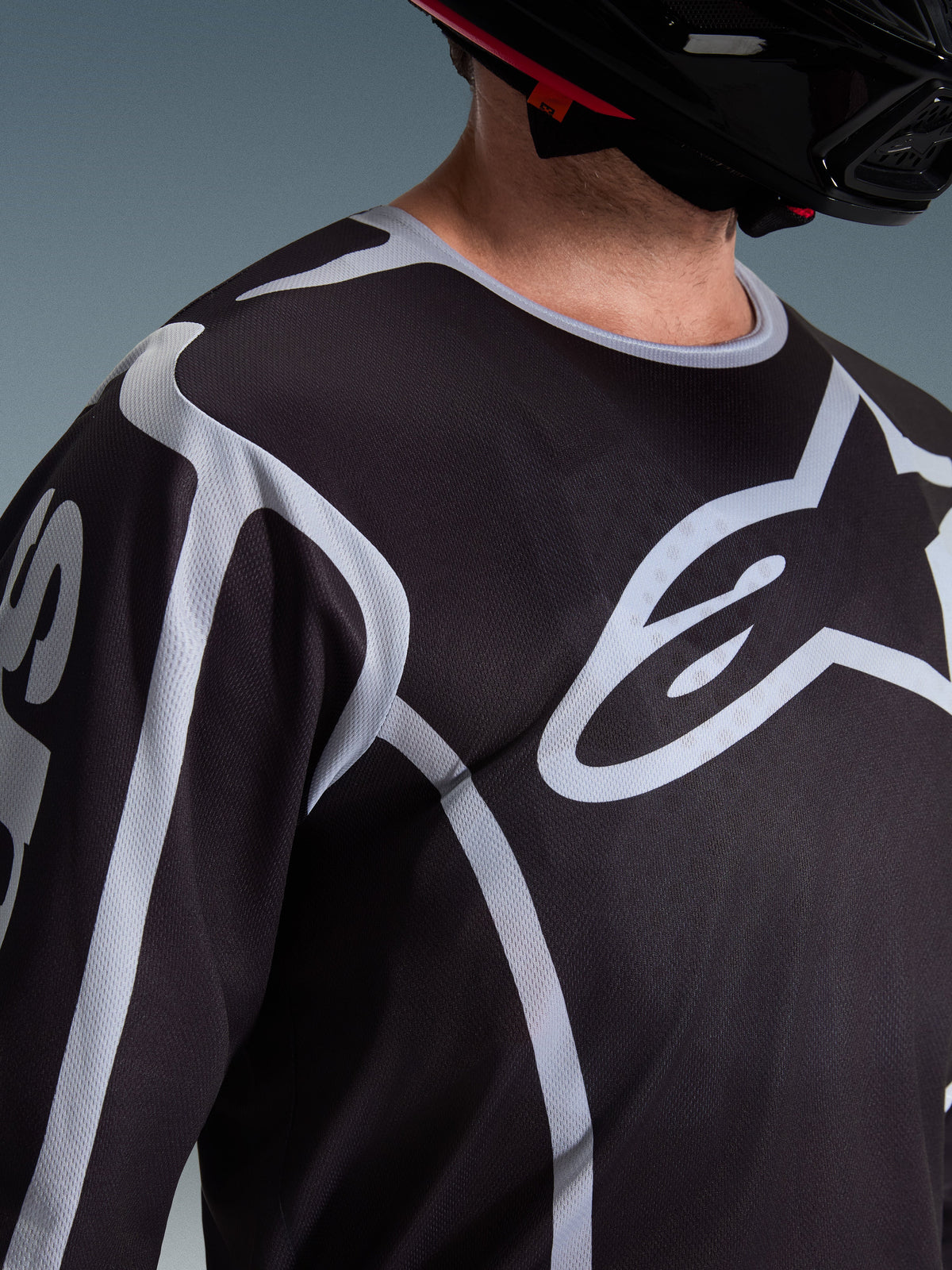Alpinestars 2026 Fluid Apex Jersey, motorcross shirt, zwart en grijs, groot Alpinestars-logo op de borst, sportkraag, gedragen met een zwarte helm, prestatiegerichte uitrusting voor off-road rijden