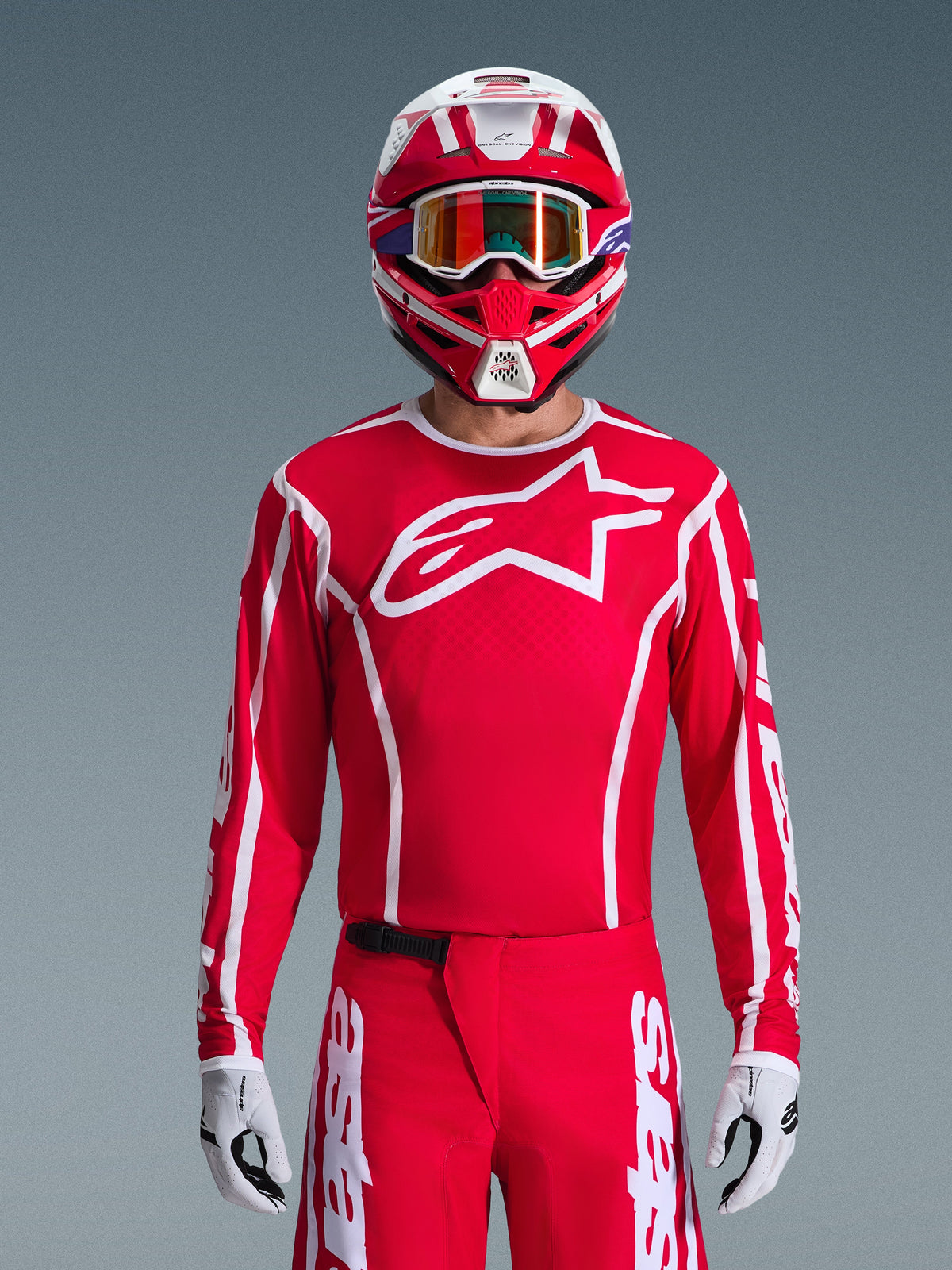 Motorcrossrijder in volledige Alpinestars 2026 Fluid Apex uitrustingsset, rode jersey met groot wit ster-logo op de borst, bijpassende rode broek met witte branding, rood-witte helm met iriserende bril, wit-zwarte handschoenen, gecoördineerde rood-witte outfit voor off-road racen